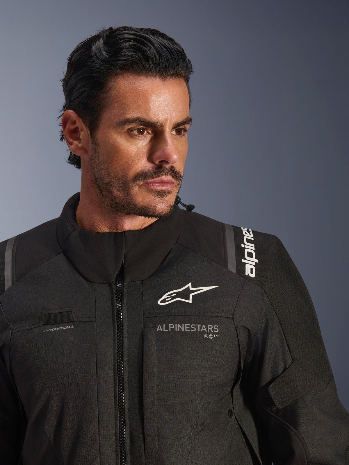 Alpinestars Andes V4 Drystar® Jacke, Schwarz, getragen von einem männlichen Model, Nahaufnahme von Brust und Schultern, mit weißen Alpinestars-Logos, Textilmaterial mit Belüftungsdetails und Trinkschlauch-Schlaufe, Adventure-Touring-Motorradausrüstung