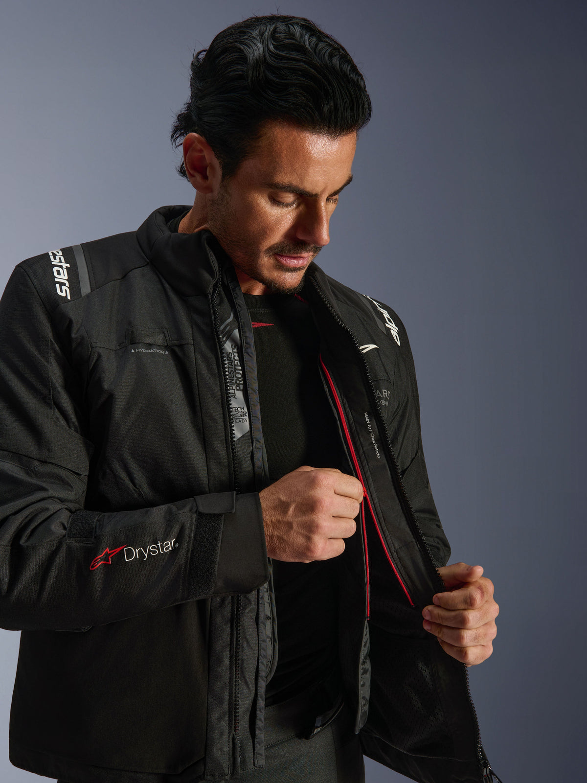 Alpinestars Andes V4 Drystar® Jacke, schwarze Adventure-Motorradjacke, Mann zeigt das interne Thermofutter und den roten Reißverschluss, mit Drystar®-Logo am Ärmel, strapazierfähiges Textilmaterial für jedes Wetter