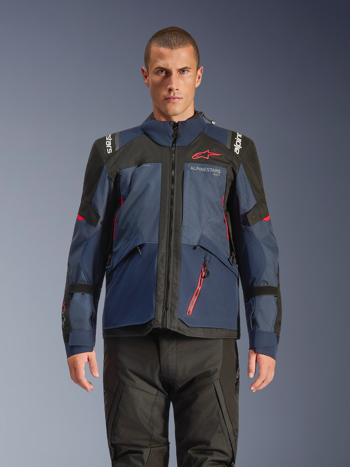 Alpinestars Andes V4 Drystar® Jacke, Adventure-Motorradjacke, Night Navy und Mood Indigo mit schwarzen Einsätzen, getragen von Model mit schwarzer Fahrhose, rotes Alpinestars-Logo auf der Brust und rotes Reißverschluss-Detail, strapazierfähige Textilkonstruktion für Allwetter-Touren.