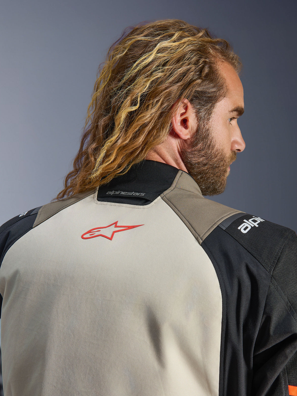 Alpinestars Andes V4 Drystar® Jacke, Farbvariante Walnut Mastic Black, Nahaufnahme des oberen Rückens und Kragens, rotes Stern-Logo auf dem mastic-farbenen Panel, Textilkonstruktion in Walnut und Schwarz, Adventure-Motorrad-Tourenbekleidung