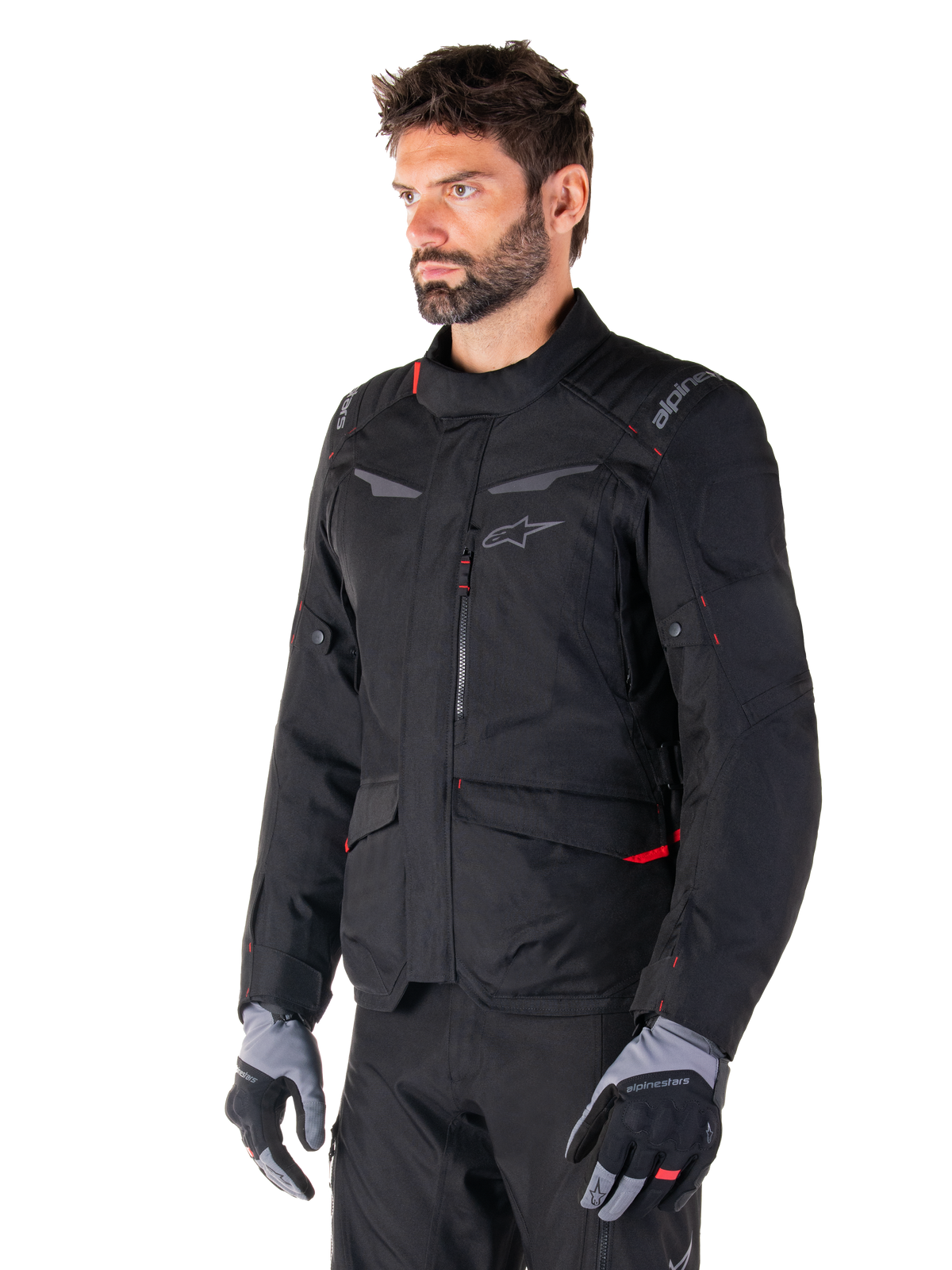 Alpinestars ST-1 Waterproof Jacket, Black with red accents, worn by a male rider with grey and black gloves, featuring a minimalist adventure touring design, cargo pockets, and subtle Alpinestars branding.