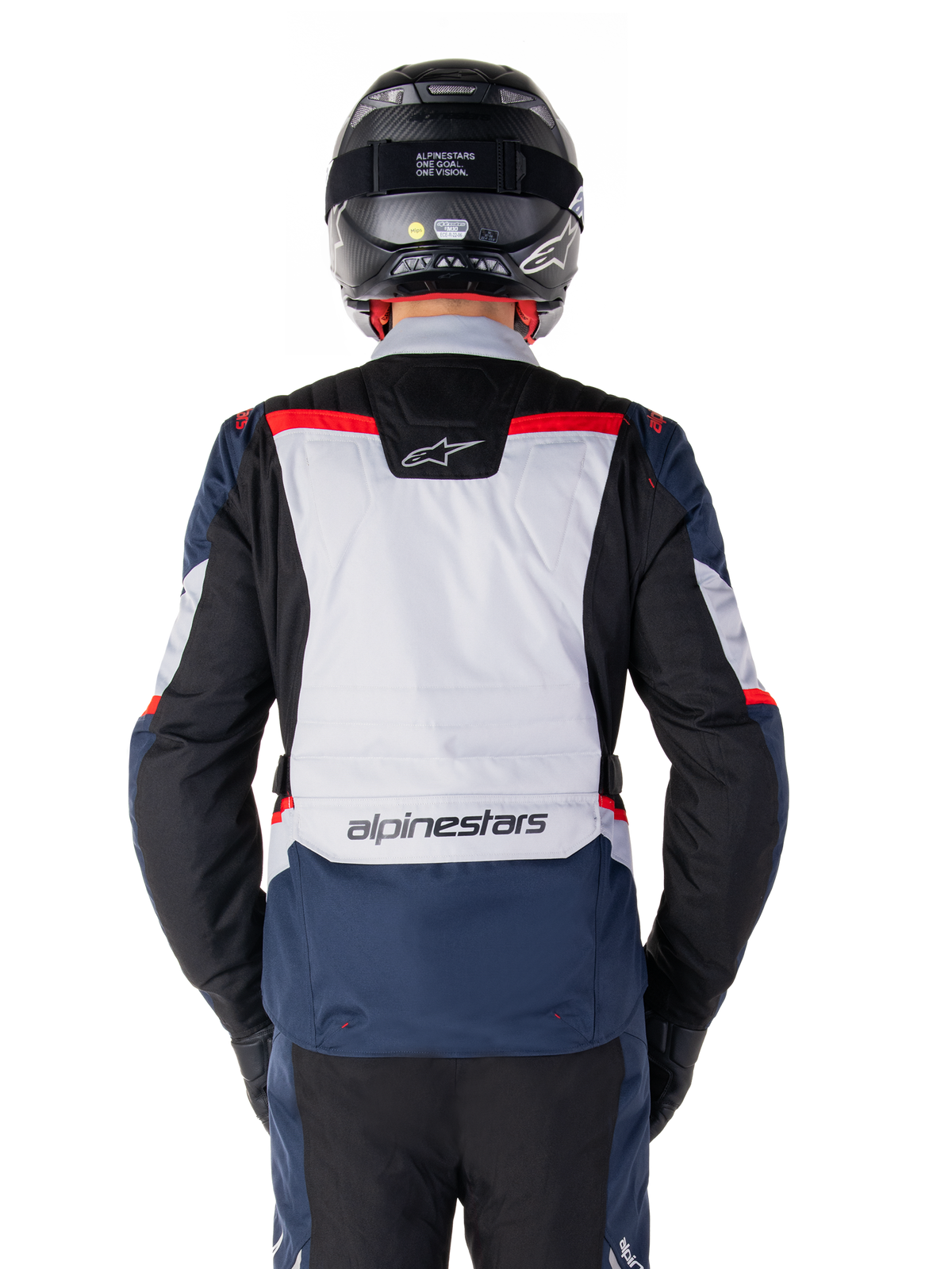 Alpinestars ST-1 wasserdichte Jacke, Dunkelblau, Schwarz und leuchtendes Rot, Rückansicht mit hellgrauer Rückenpartie und Branding, Adventure-Touren-Motorradjacke getragen mit schwarzem Helm und Handschuhen, stromlinienförmiges Design für Fahrten bei jedem Wetter