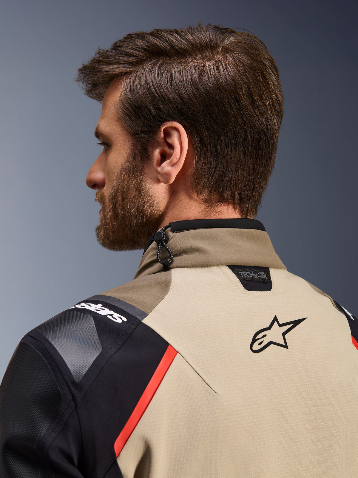 Alpinestars Andes Pro Drystar® XF Jacke in Walnut Aluminum, Nahaufnahme der Rückansicht von Kragen und oberem Schulterbereich, mit Alpinestars-Logo, Tech-Air®-Kompatibilitäts-Branding, roten Akzenten und Kordelzug-Verstellsystem am Nacken.