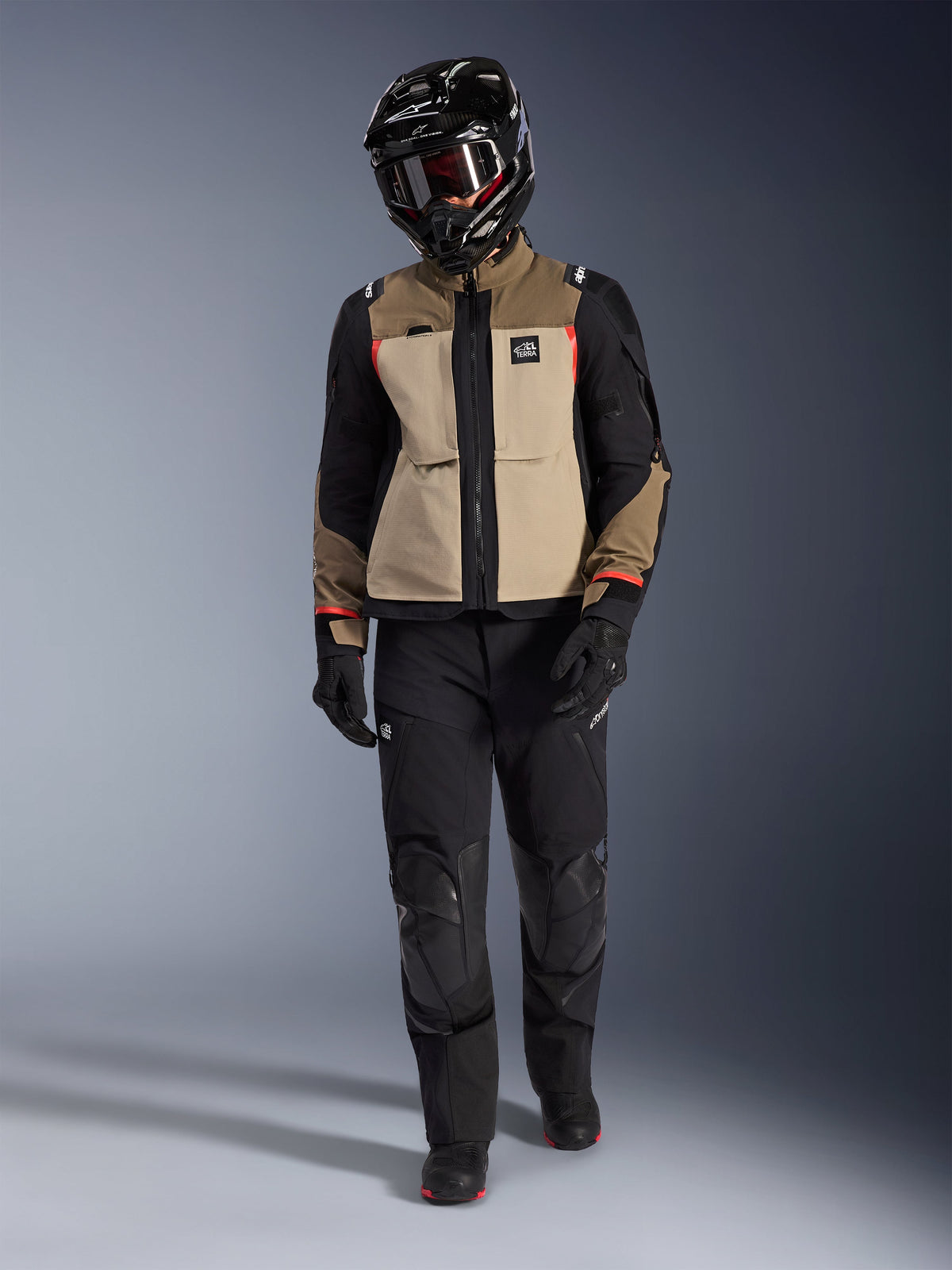 Alpinestars Andes Pro Drystar® XF Jacke in Walnut Aluminum, kombiniert mit schwarzer Adventure-Hose, schwarzen Handschuhen und einem schwarzen Full-Face-Helm mit Brille, rote Highlights und All Terra-Branding, professionelles Adventure-Touring-Setup