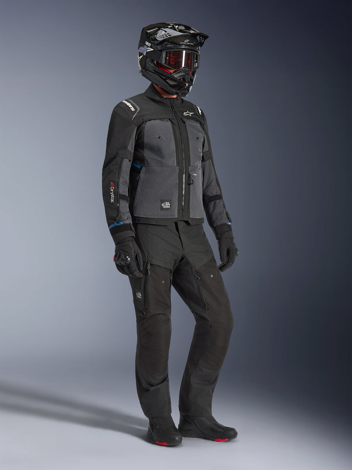 Model trägt die Alpinestars Cusco Drystar® Jacke in Schwarz und Deep Gray, kombiniert mit kompletter Motorrad-Ausrüstung inklusive schwarzem Helm, passender technischer Hose, Handschuhen und Stiefeln, mit Ripstop- und Softshell-Konstruktion für Road- und Adventure-Touren