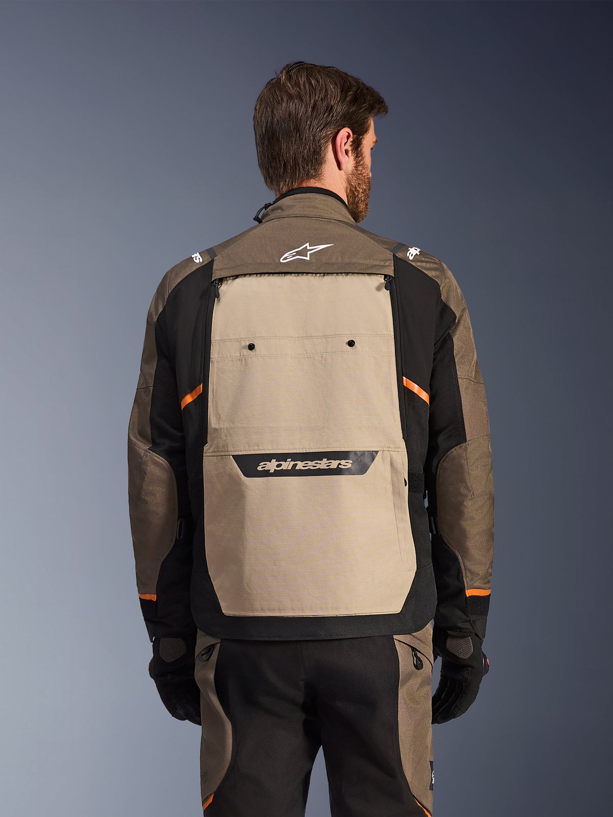 Alpinestars Cusco Drystar® Jacke, Walnut Aluminum Black, Rückansicht, mit einem großen beigen Rückenpanel mit schwarzem Logo, orangefarbenen Akzenten, getragen mit passender Hose und Handschuhen, entwickelt für Adventure-Touring.