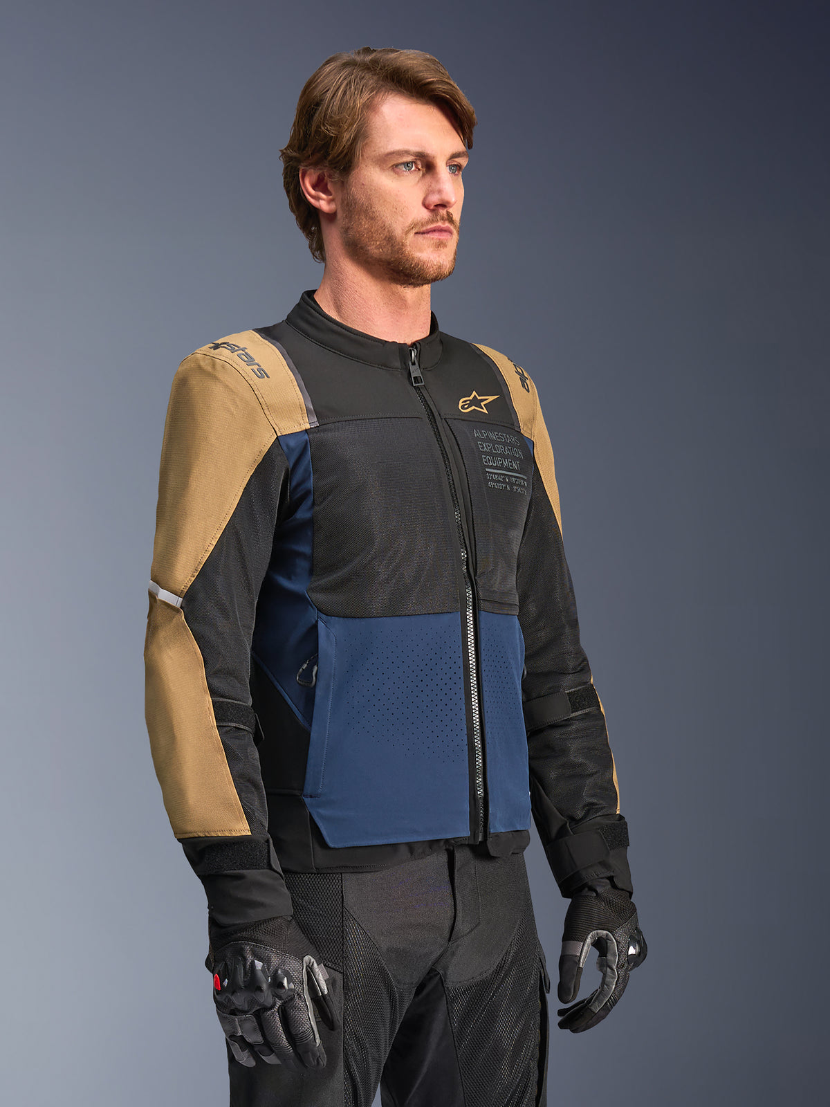Alpinestars ST-2 Air Jacke, Motorradjacke, Dunkelblau, Dunkles Khaki und Schwarz, mit Mesh-Belüftungseinsätzen für hohen Luftstrom und „Alpinestars Exploration Equipment“-Branding, getragen mit schwarzen Motorradhandschuhen, modernes Adventure-Touring-Design
