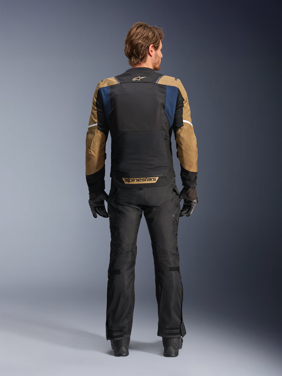 Alpinestars ST-2 Air Jacke in Tiefblau, Dunklem Khaki und Schwarz, Rückansicht am Modell mit großem Mesh-Rückenteil und khakifarbenen Ärmeln mit weißen Streifen, kombiniert mit schwarzer technischer Motorradhose und Handschuhen für Adventure-Touring.