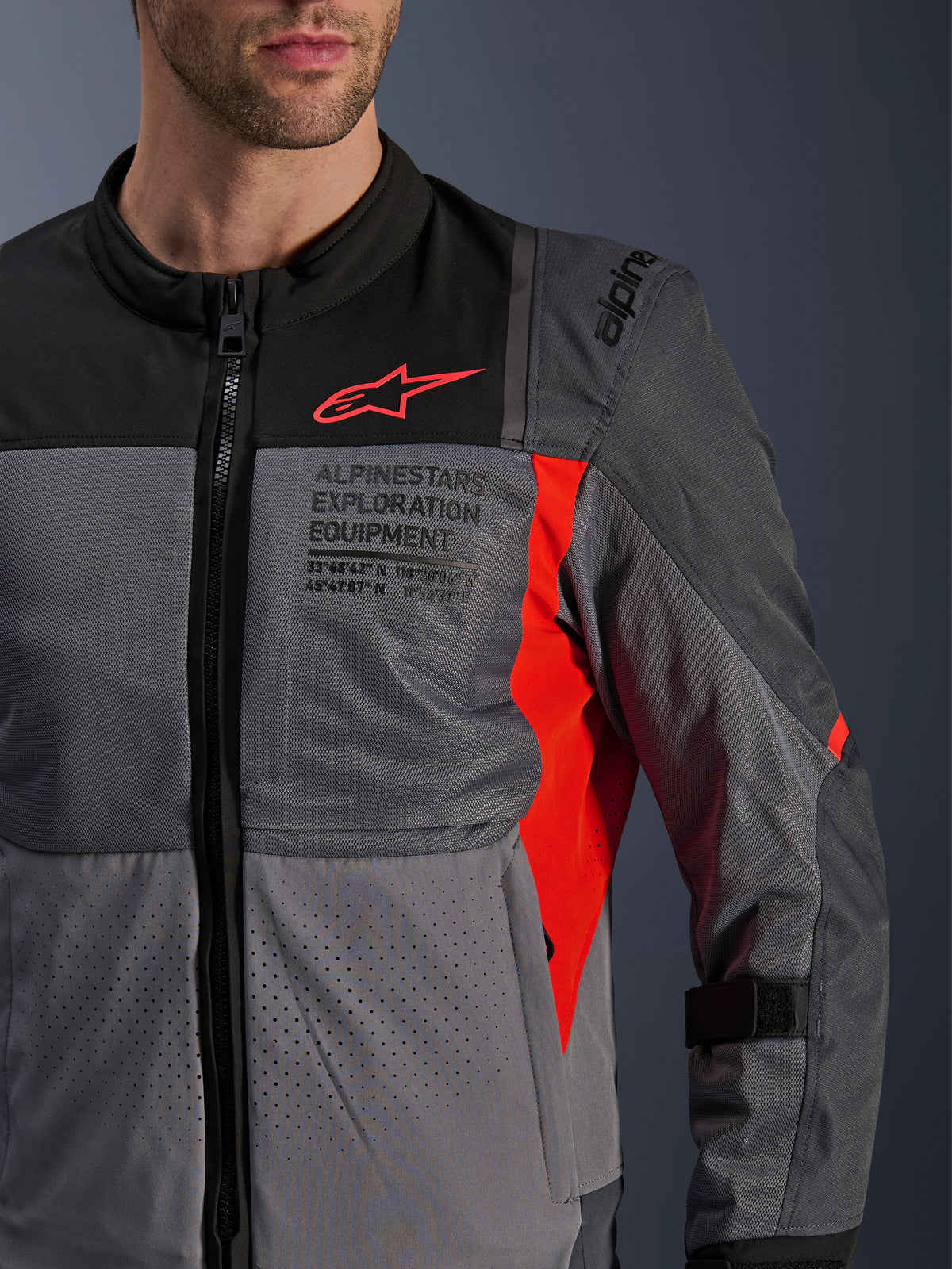 Alpinestars ST-2 Air Jacke, Herren-Motorradjacke für Touring, Grau und Rot, Nahaufnahme mit atmungsaktiven Mesh-Einsätzen, laserperforiertem Textil und markantem Exploration Equipment Branding.