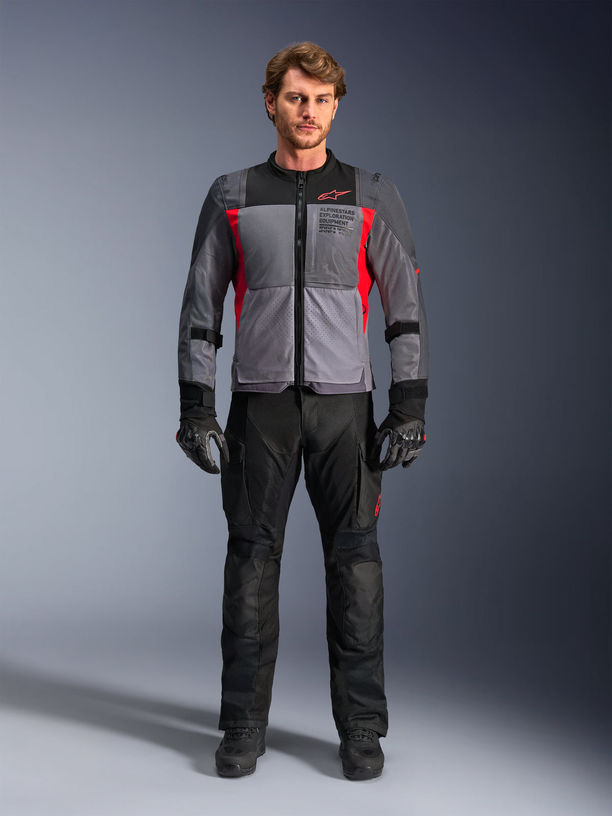 Alpinestars ST-2 Air Jacke, Adventure-Touring-Motorradjacke für Herren, Grau und Rot, mit großflächiger Mesh-Belüftung und Exploration-Branding, getragen von einem Model mit schwarzer Motorradhose.