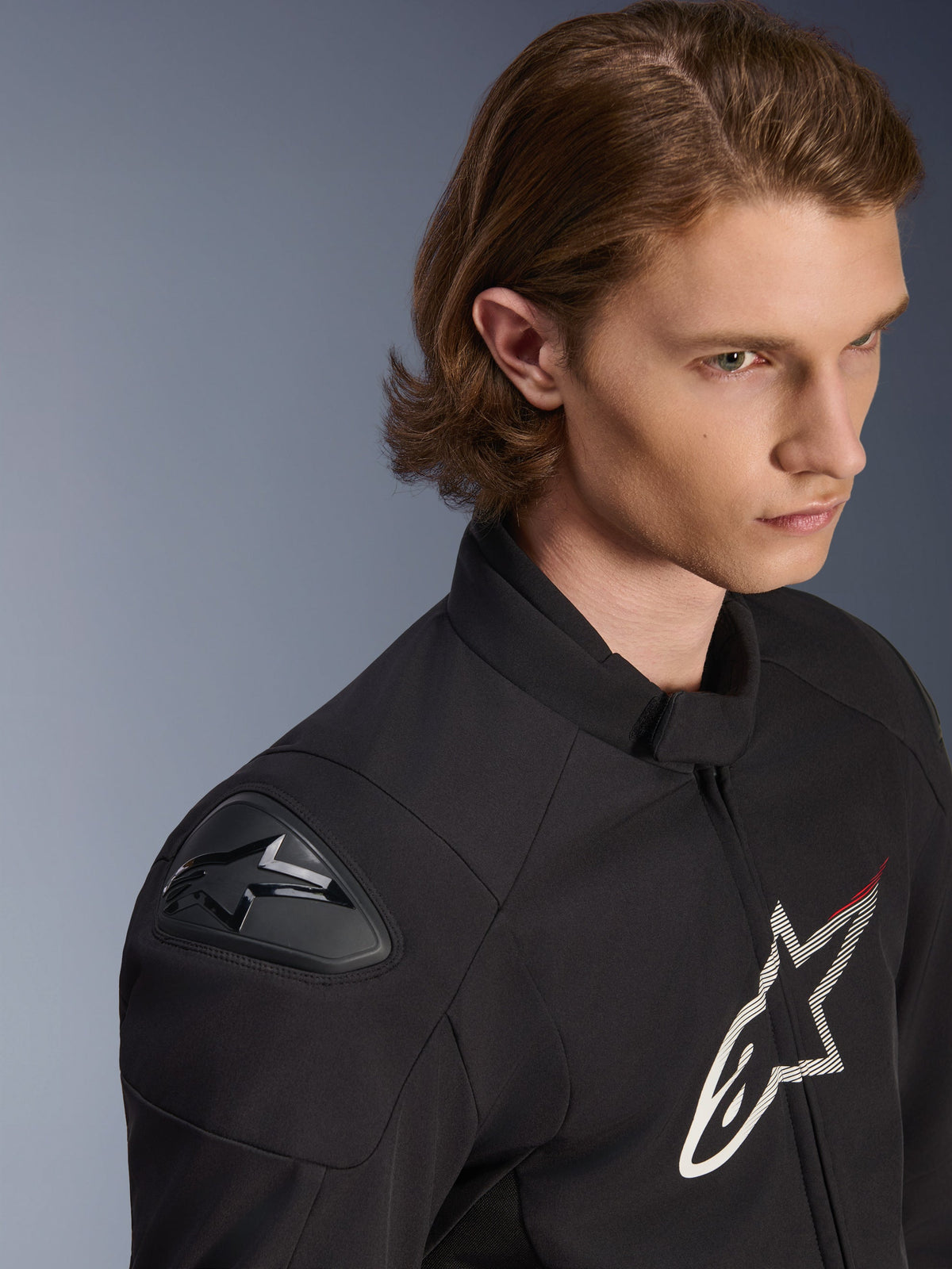 Alpinestars SMX Wasserdichte Jacke, Schwarz mit weißen und roten Akzenten, Nahaufnahme an einem männlichen Model, mit externen DFS Lite Schulterschleifern und großem Stern-Logo auf der Brust, sportliche Motorradbekleidung