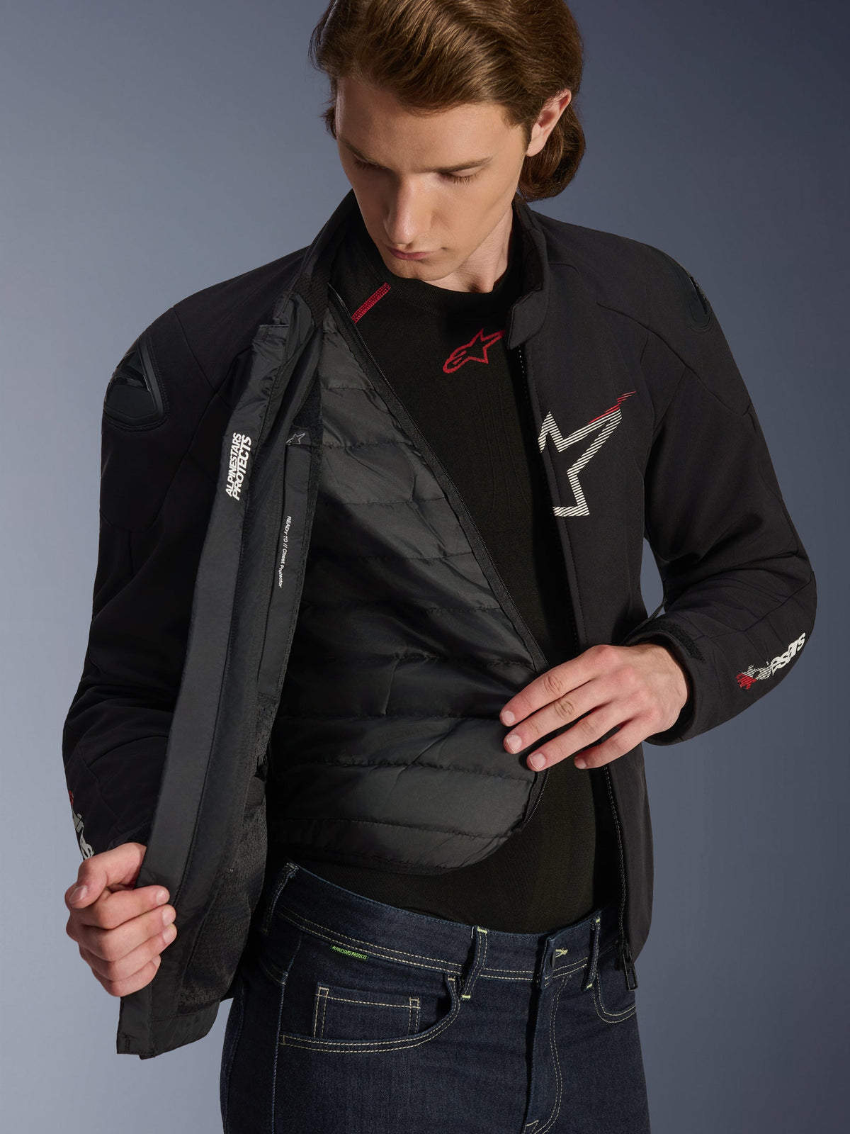Alpinestars SMX Waterproof Jacke in Schwarz, Weiß und leuchtendem Rot, getragen von einem Mann und geöffnet zur Ansicht des gesteppten, herausnehmbaren Thermofutters, mit externen DFS Lite Schultern und weißen Logo-Details, Performance-Motorradbekleidung für die Straße