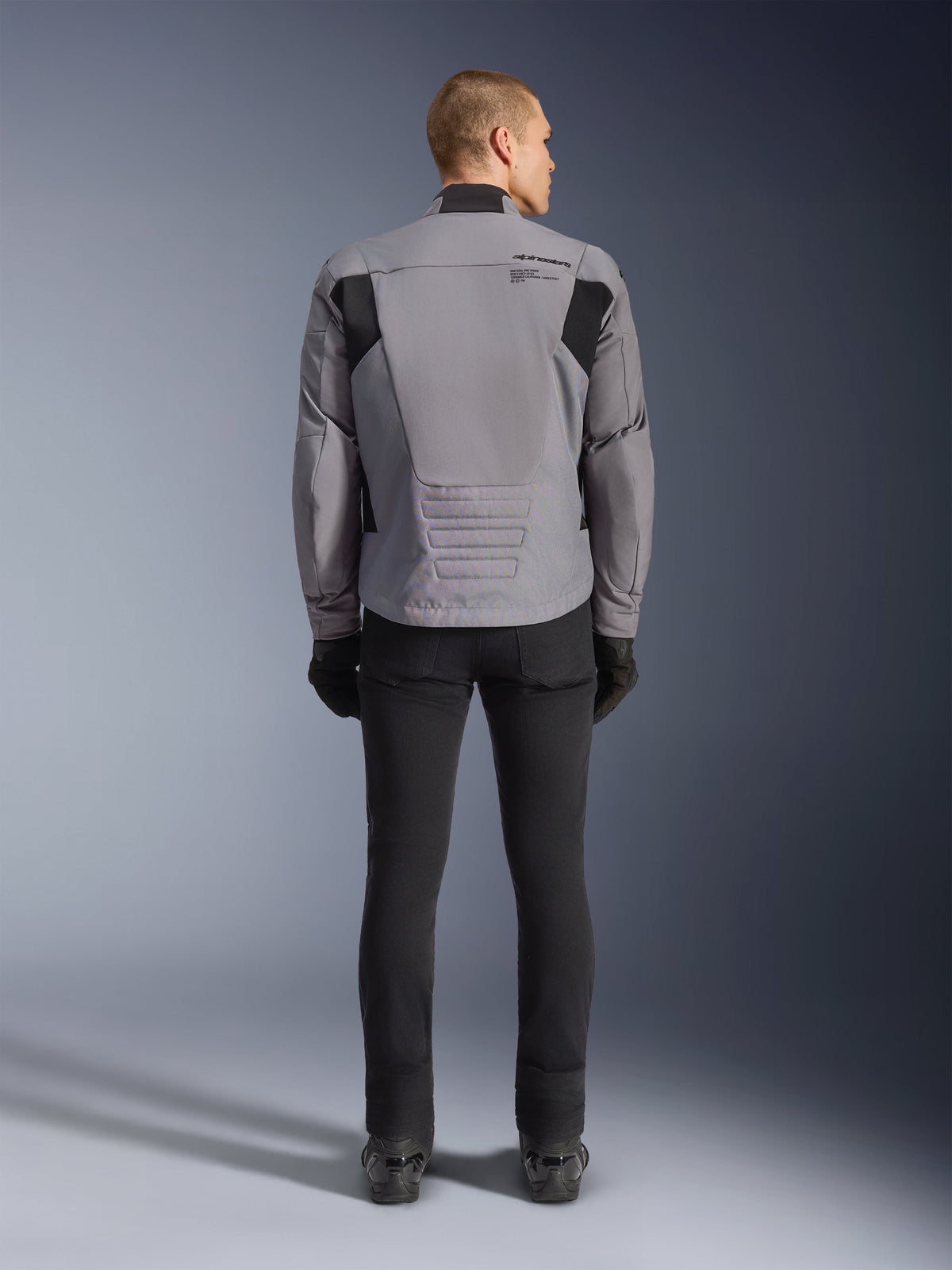Alpinestars SMX Wasserdichte Jacke, Rückansicht, Dunkelgrau und Schwarz, mit schwarzen Textilpaneelen an den Schultern und einem sportlichen Design, kombiniert mit schwarzer Hose und Handschuhen für einen kompletten Motorrad-Look