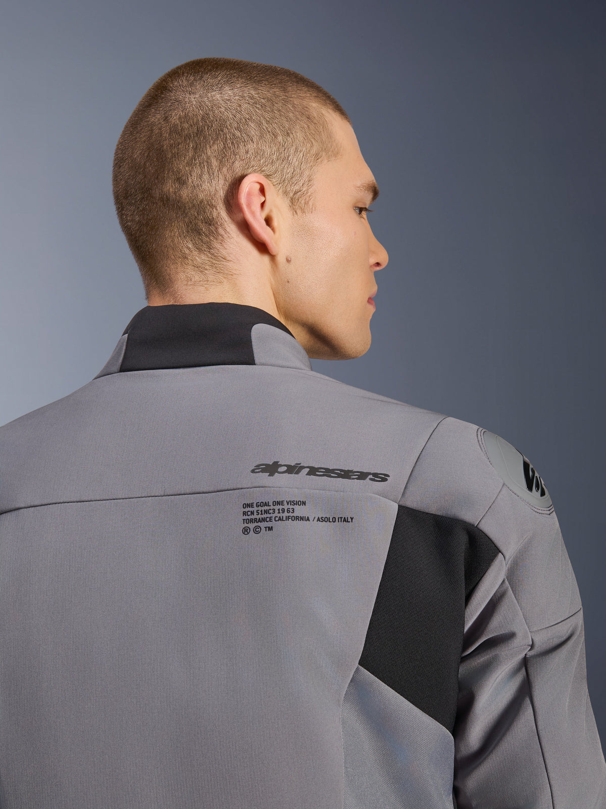 Alpinestars SMX Waterproof Jacke in Dunkelgrau-Schwarz, Nahaufnahme des Rücken- und Schulterbereichs mit Alpinestars-Branding und DFS lite Schulterschutz, getragen von einem männlichen Model