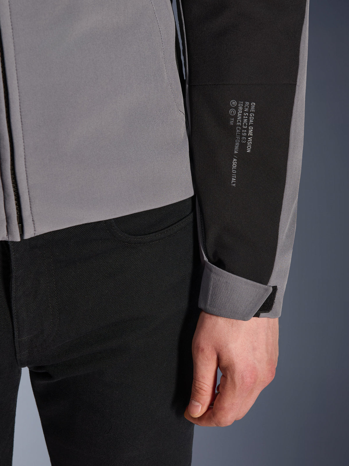 Alpinestars SMX Wasserdichte Jacke, Dunkelgrau und Schwarz, Nahaufnahme des Ärmels mit weißem Textaufdruck zur Marken-Historie, verstellbares Klettverschluss-Bündchen, sportliches Textildesign für Motorradfahrten bei jedem Wetter