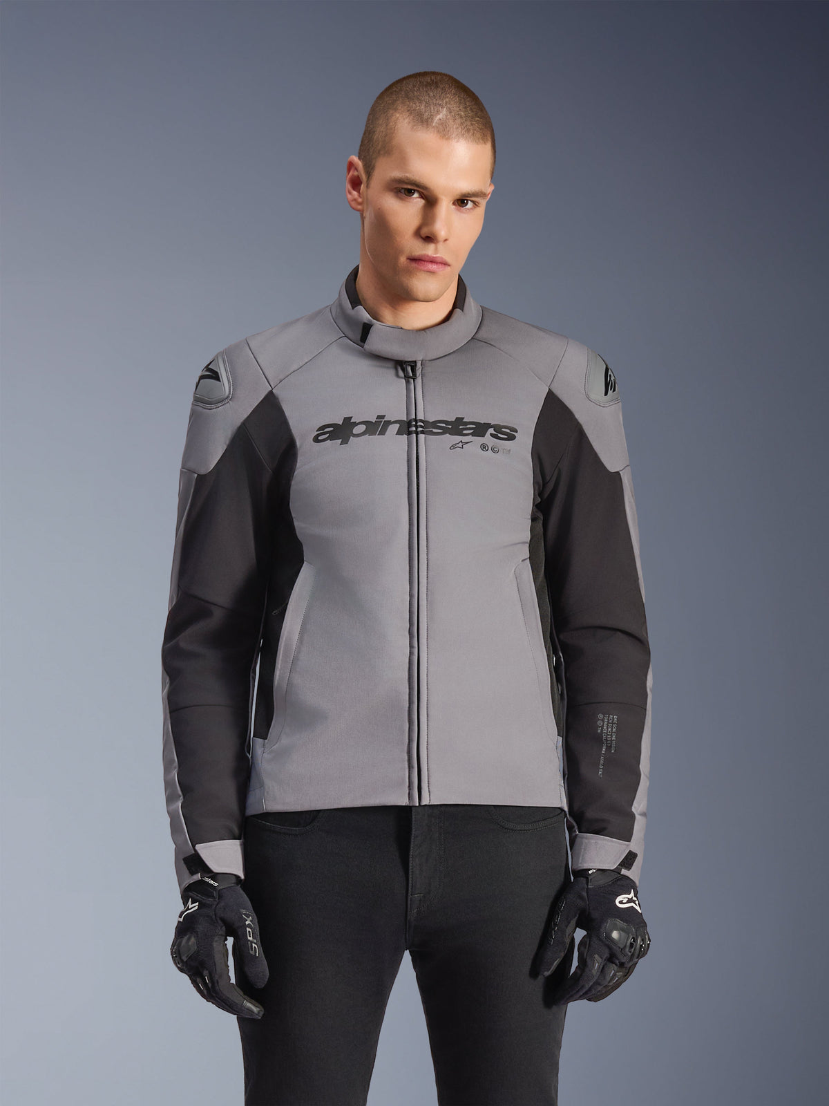 Alpinestars SMX Wasserdichte Jacke, sportliche Straßenmotorradjacke, Dunkelgrau und Schwarz, mit hohem Kragen und DFS Lite Schulterschleifern, getragen mit schwarzen SMX-Handschuhen, schlanke sportliche Passform für das Fahren bei jedem Wetter