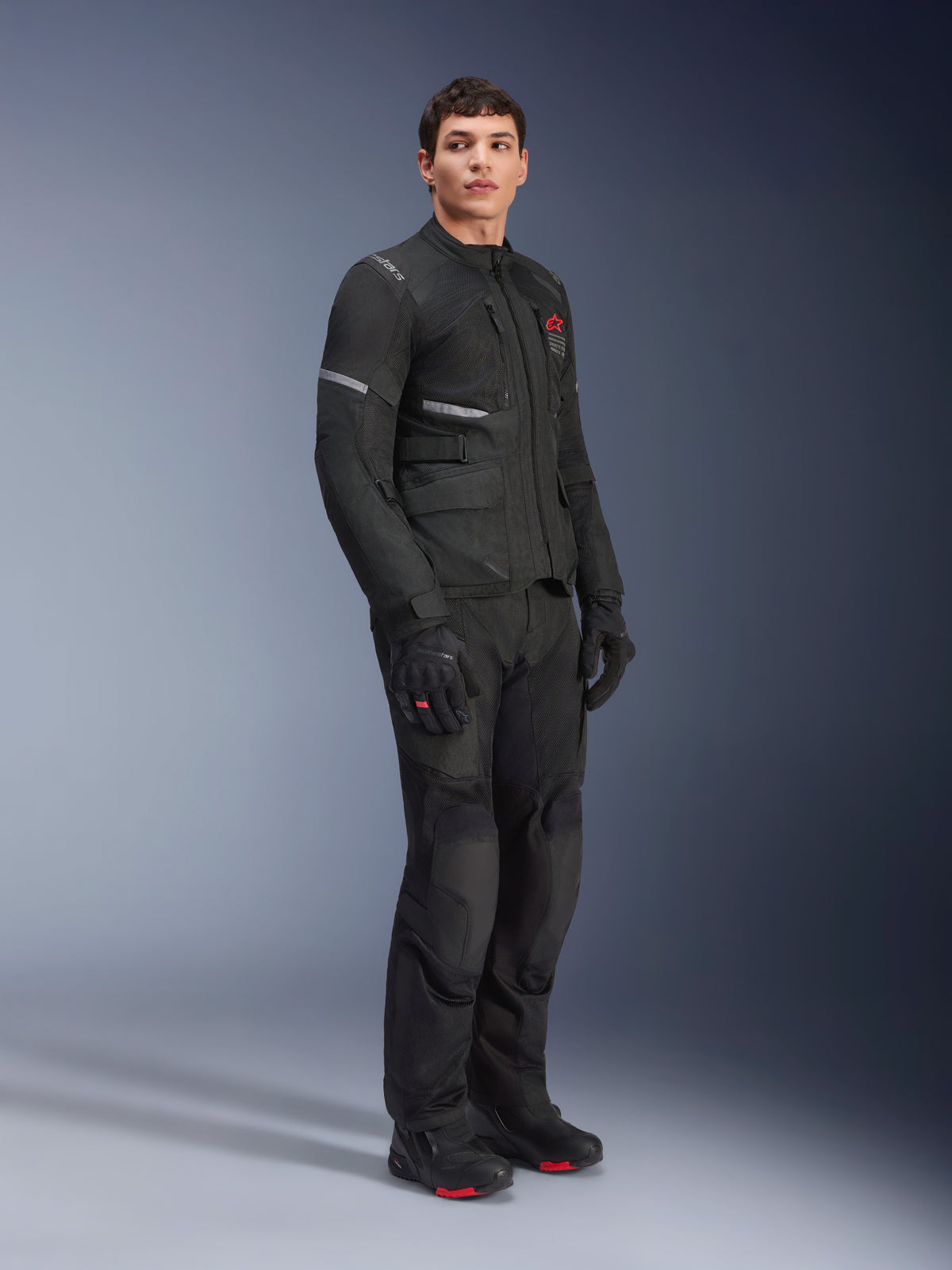Alpinestars Andes Air Drystar® Jacke und Hose, Adventure-Touring-Outfit, Schwarz, Ganzkörperansicht eines Models in koordinierter Motorradausrüstung inklusive Handschuhen und Stiefeln, mit atmungsaktiven Mesh-Einsätzen und roten Marken-Akzenten.