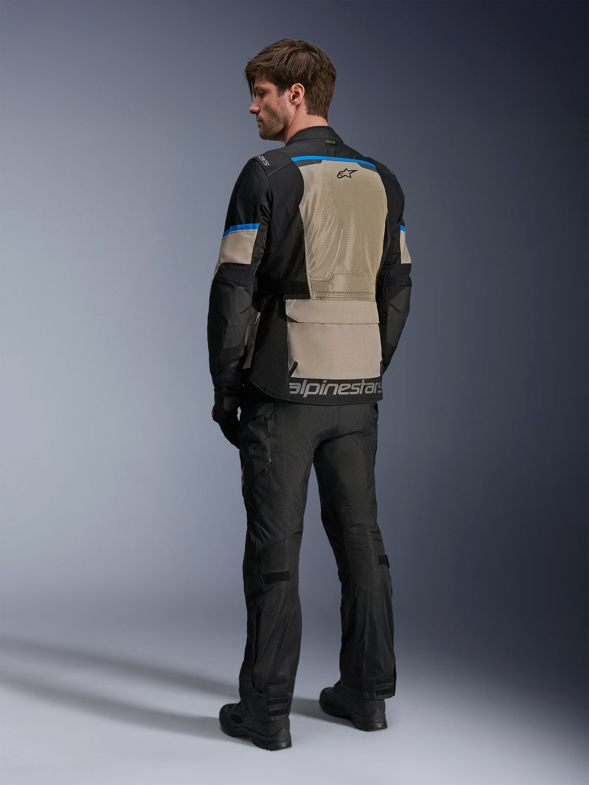 Alpinestars Andes Air Drystar® Jacke, Schwarz, Laurel Gray und Bright Blue, Rückansicht mit großem Mesh-Belüftungspanel am Rücken, Logo am unteren Saum, getragen mit schwarzer Motorradhose und Stiefeln.