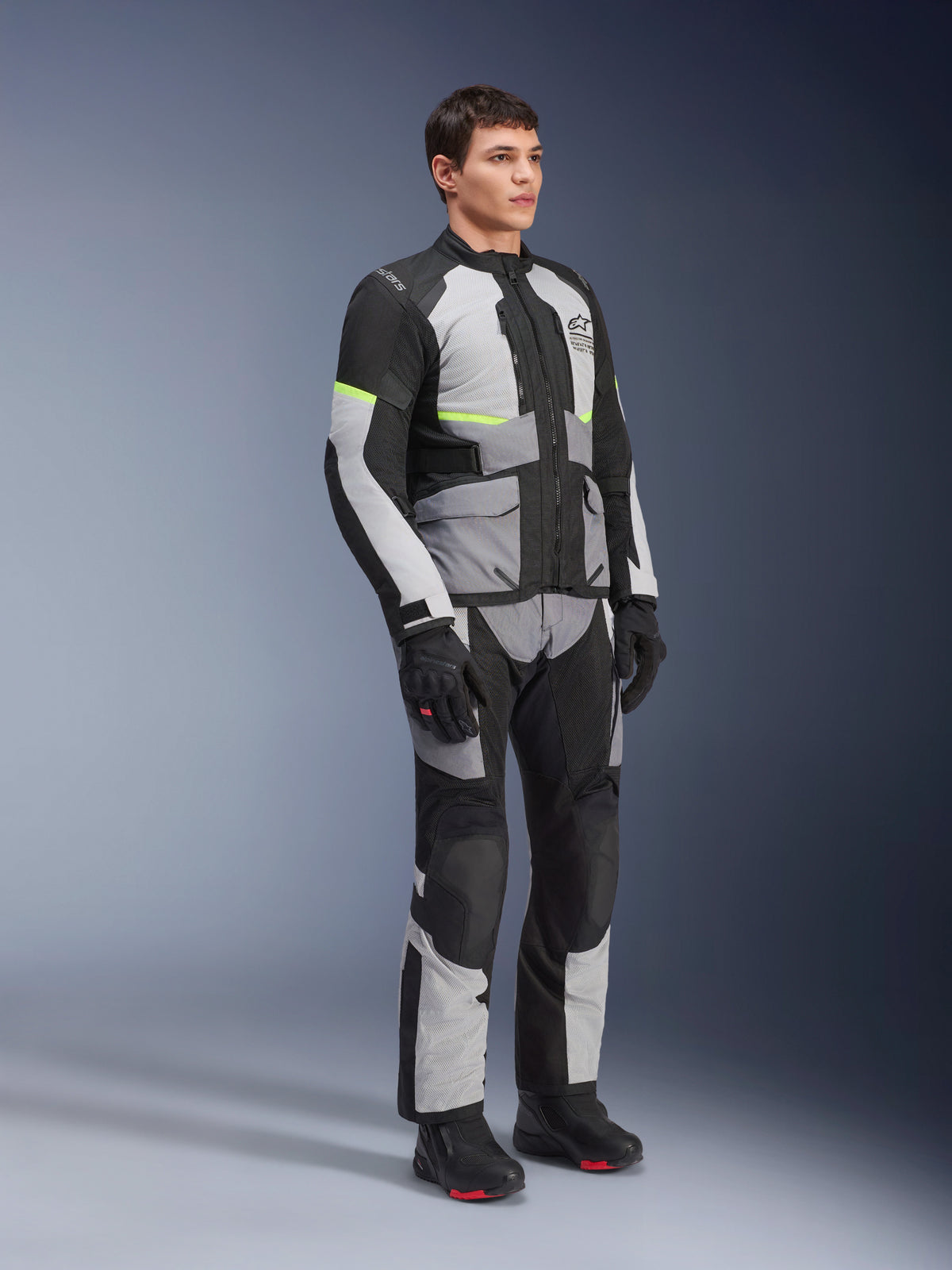 Alpinestars Andes Air Drystar® Jacke, Ice Gray, Dunkelgrau und Schwarz, getragen von einem Modell in einem kompletten Adventure-Touring-Outfit mit passender Hose und schwarzen Stiefeln, mit Mesh-Belüftung, Neon-Akzenten und Alpinestars-Branding.