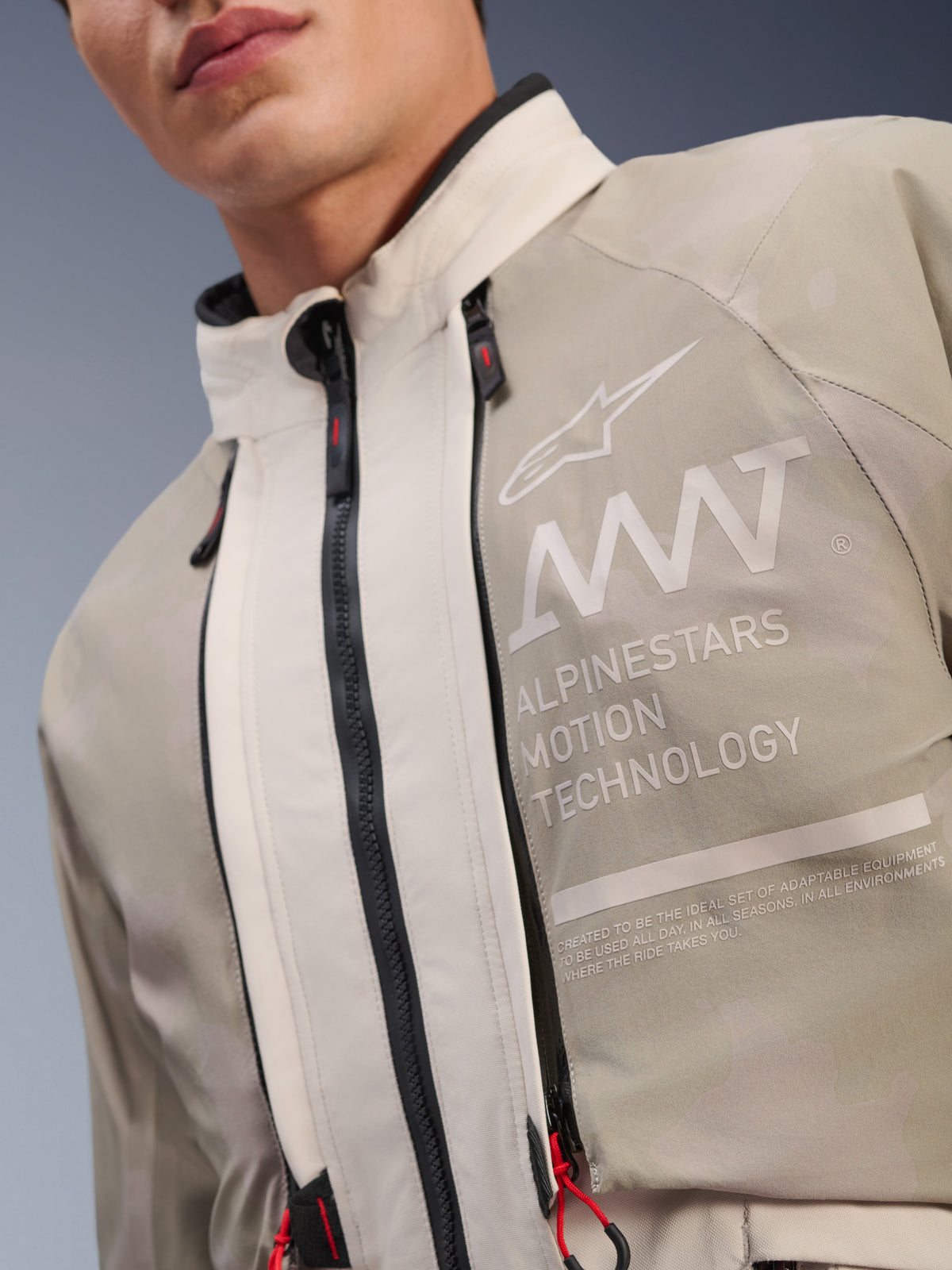 Alpinestars AMT-10LAB Drystar® XF Jacke, White Sand Aluminum Camo, Nahaufnahme der Brustpartie mit AMT Alpinestars Motion Technology Branding, wasserdichten Reißverschlüssen mit roten Zuglaschen und texturiertem, abenteuertauglichem Textilgewebe.