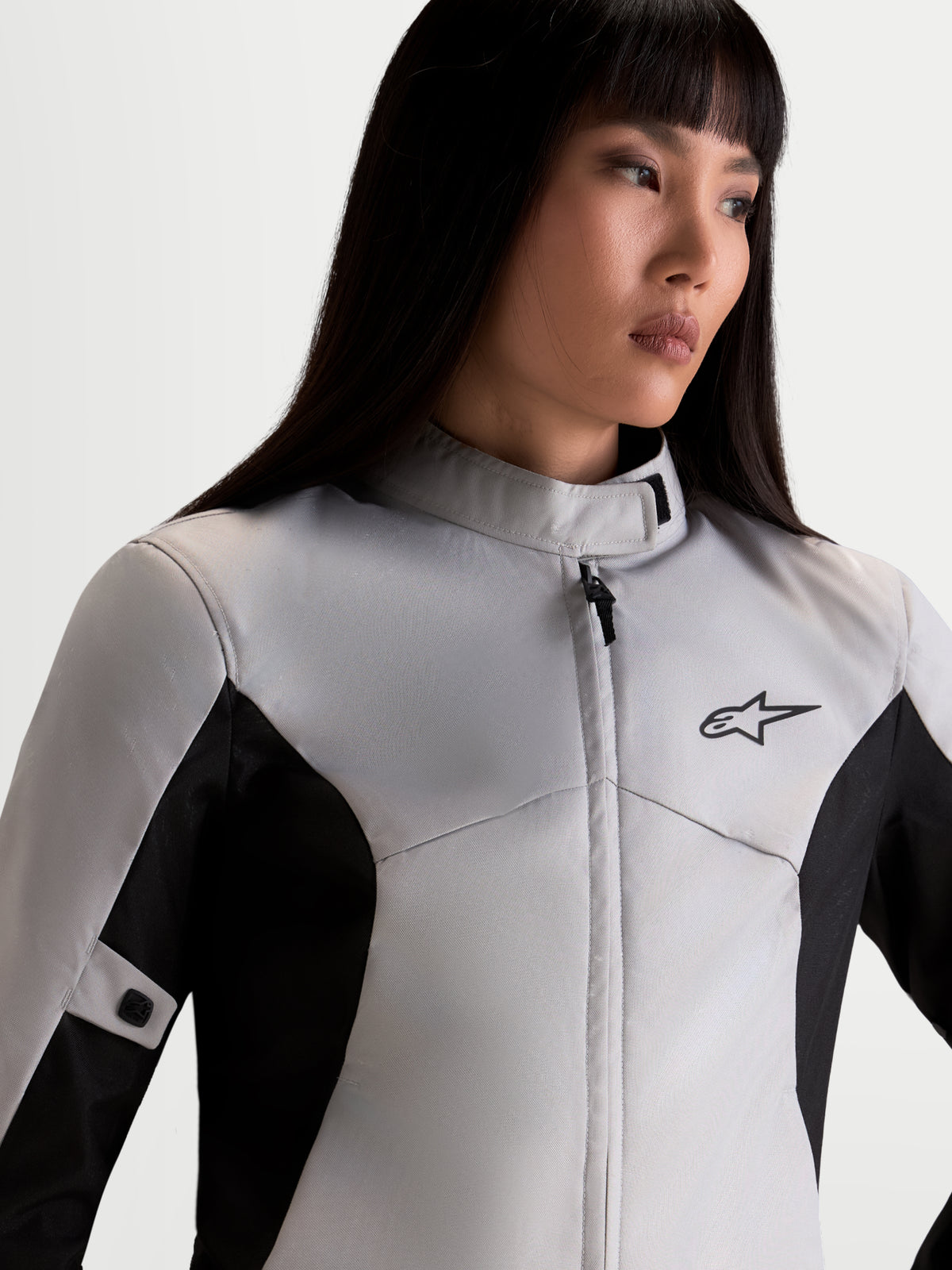 Alpinestars Stella C-1 Waterproof Jacke, urbane Damen-Motorradjacke in Eisgrau und Schwarz, Nahaufnahme des Oberkörpers mit hohem Kragen, wasserdichter Textilkonstruktion und A-Star-Logo am Model