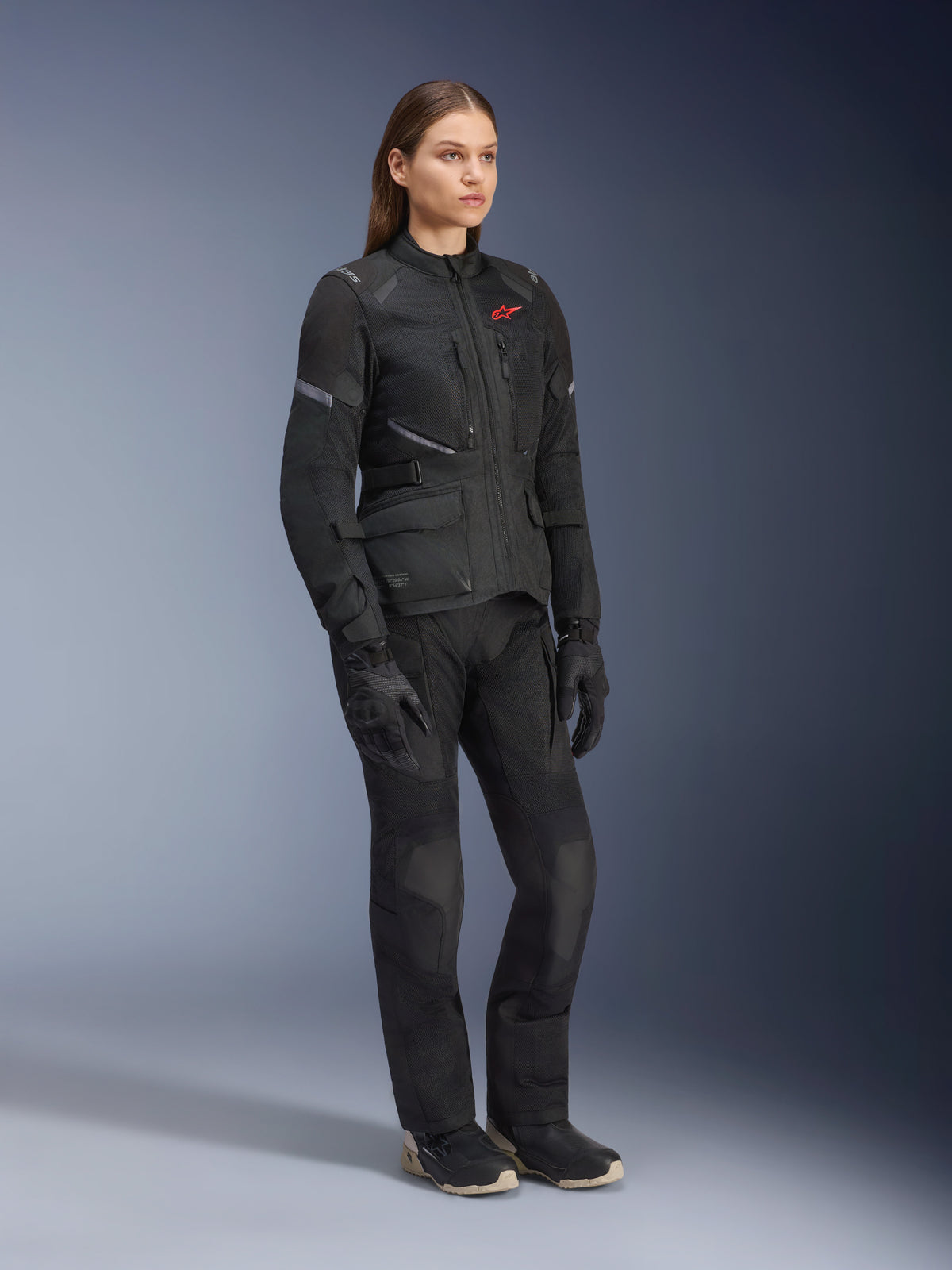 Frau in Alpinestars Stella Andes Air Drystar® Jacke, schwarze Textil-Adventure-Tourenjacke, kombiniert mit passender schwarzer Hose und Handschuhen, mit großen Mesh-Belüftungseinsätzen und rotem Logo, abgestimmtes Outfit für Motorradfahrerinnen