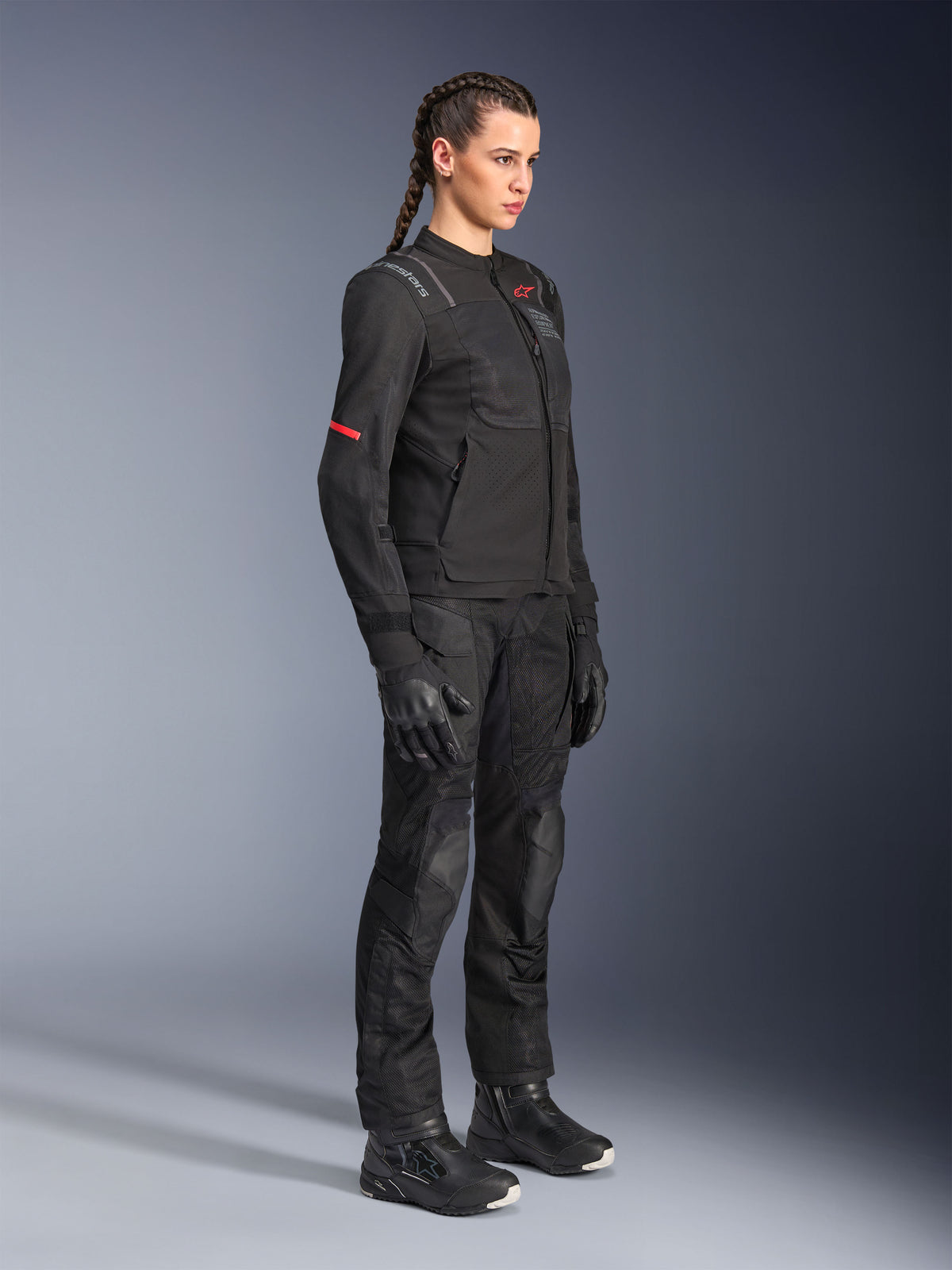 Motorradfahrerin trägt die Alpinestars Stella Andes Air Drystar® Hose in Schwarz, eine Textil-Abenteuerhose mit Mesh-Belüftungseinsätzen, kombiniert mit einer passenden Stella Jacke, Handschuhen und Stiefeln für ein komplettes Motorrad-Tourenoutfit.