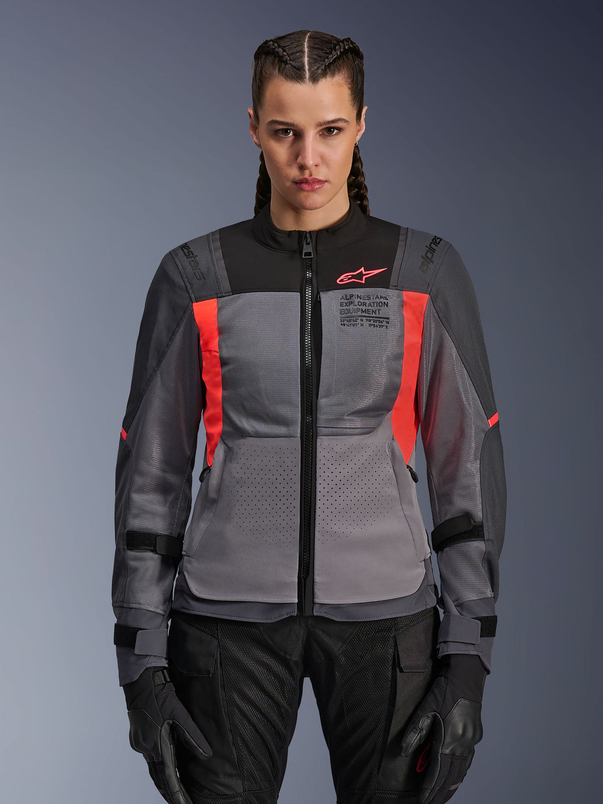 Alpinestars Stella ST-2 Air Jacke, Damen-Motorradjacke, Dunkelgrau und Fluo-Koralle, Modell trägt belüftete Textiljacke mit Mesh-Einsätzen, leuchtende korallenfarbene Akzente und Branding auf der Brust, moderner Adventure-Fahrstil