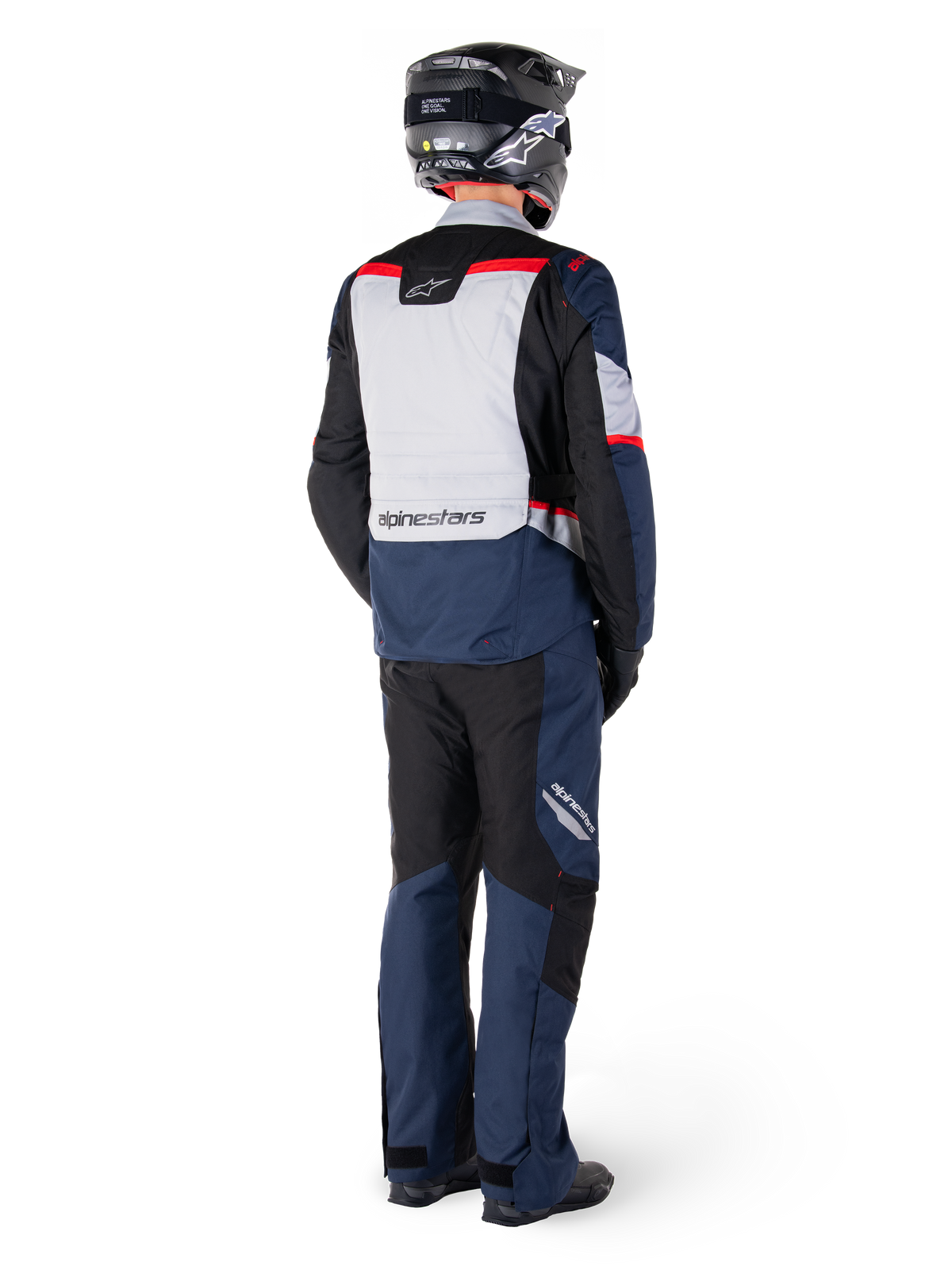 Rear view of a motorcycle rider wearing Alpinestars ST-1 Waterproof Pants and matching jacket in Dark Blue Black and Bright Red, adventure touring gear with textile panels and reflective accents, paired with a black helmet and boots.
