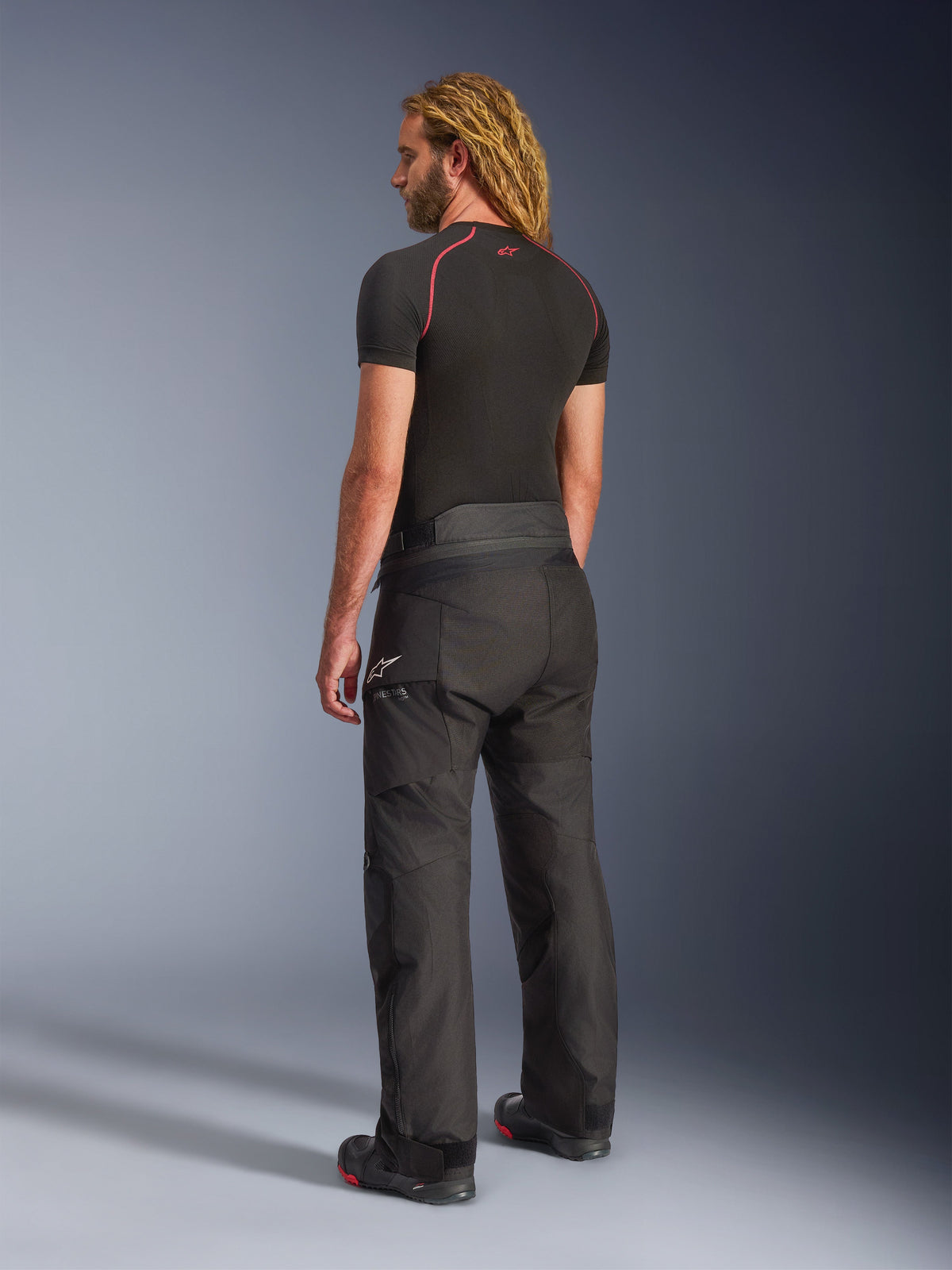 Alpinestars Andes V4 Drystar® Hose - Lang, Adventure-Motorradhose, Schwarz, Dreiviertel-Rückansicht am Modell, strapazierfähiges Textildesign mit verstärkten Gesäß- und Knieeinsätzen, mit Alpinestars Stern-Logo, getragen mit schwarzem Base Layer und Motorradstiefeln.