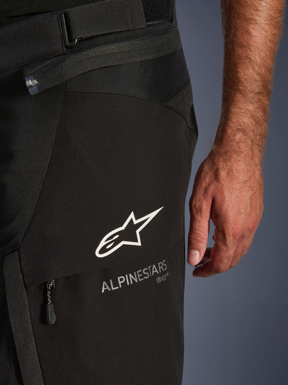 Alpinestars Andes V4 Drystar Hose, Motorrad-Abenteuerhose, Schwarz, Nahaufnahme des oberen Oberschenkelbereichs mit weißem Alpinestars Stern-Logo und Schriftzug, Taillenverstellriemen und Reißverschlusstaschen-Detail.