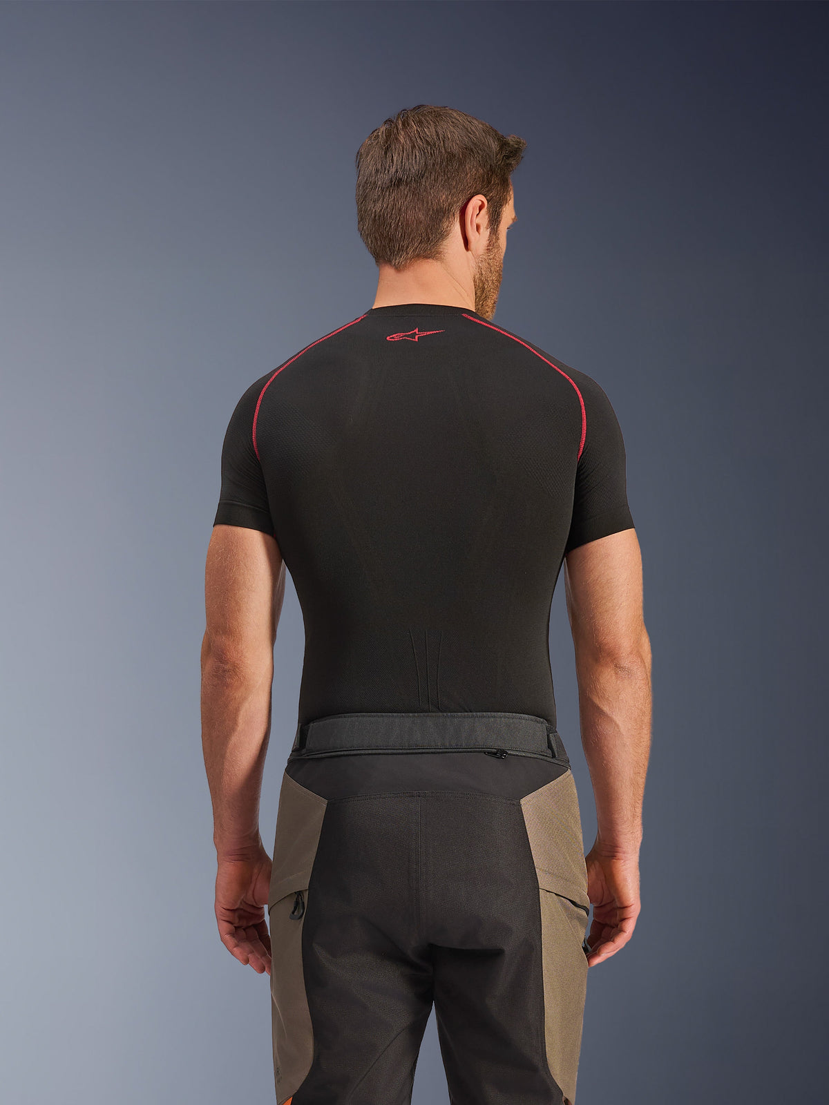 Alpinestars Cusco Drystar® Hose, Adventure-Motorradhose, Walnut Black, Rückansicht mit Taillendetails und Color-Blocking-Design, getragen mit einem schwarzen kurzärmeligen Base-Layer mit roten Nähten und Logo