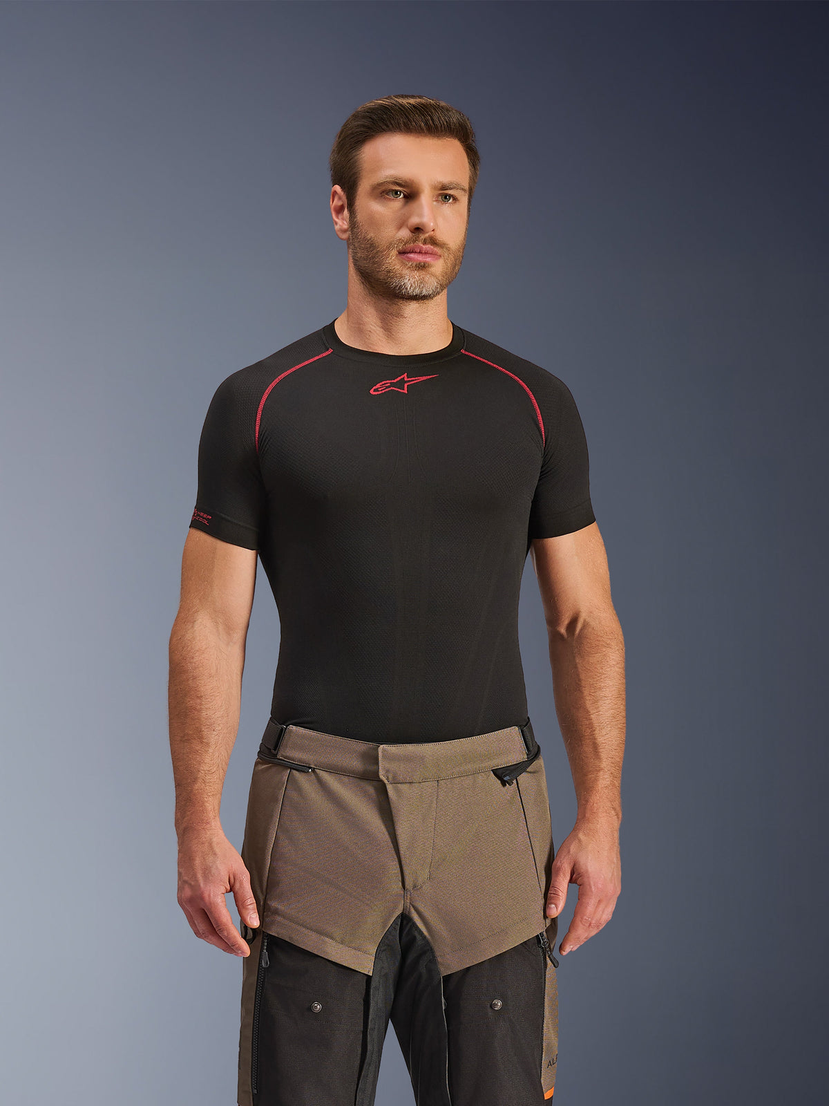 Alpinestars Cusco Drystar® Hose, Adventure-Motorradhose in Walnut Black, getragen von einem Model mit einem schwarzen Alpinestars Base-Layer-Shirt, mit einem zweifarbigen braun-schwarzen Textildesign und verstärkten Einsätzen für Touren.