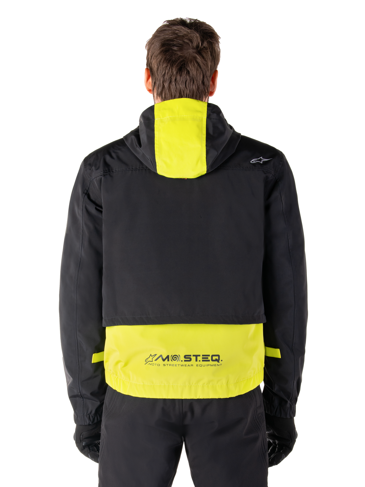 Alpinestars Mootant Waterproof Parka, Motorradjacke, Lime Punch und Schwarz, Rückansicht mit Kapuzendesign und reflektierendem MO.ST.EQ. Branding am unteren Rücken, getragen mit schwarzer Motorradhose und Handschuhen.