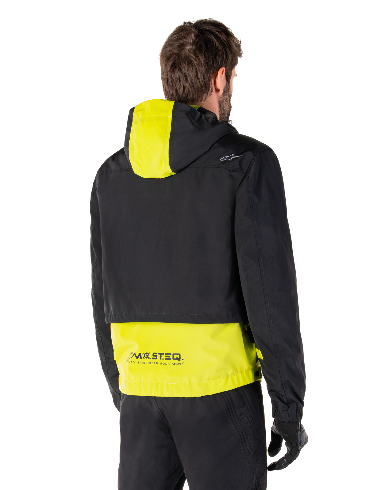 Alpinestars Mootant Waterproof Parka, Rückansicht, Lime Punch und Schwarz, mit schwarzem Oberkörper, limonengelbem Kapuzeneinsatz und unterem Rücken, MO.ST.EQ. Branding am Saum, getragen mit schwarzer Motorradhose und Handschuhen, moderne urbane Motorradjacke