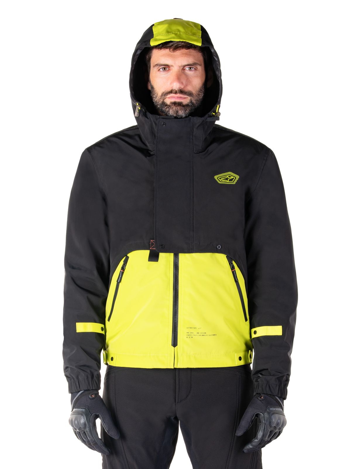 Alpinestars Mootant Waterproof Parka, Motorradjacke in Lime Punch Black, Vorderansicht, modulares 3-in-1-Design mit schwarzem Oberteil und leuchtend limonengrünem Unterteil, Kapuze mit Kordelzug und Brustlogo, getragen mit schwarzer Hose und Motorradhandschuhen