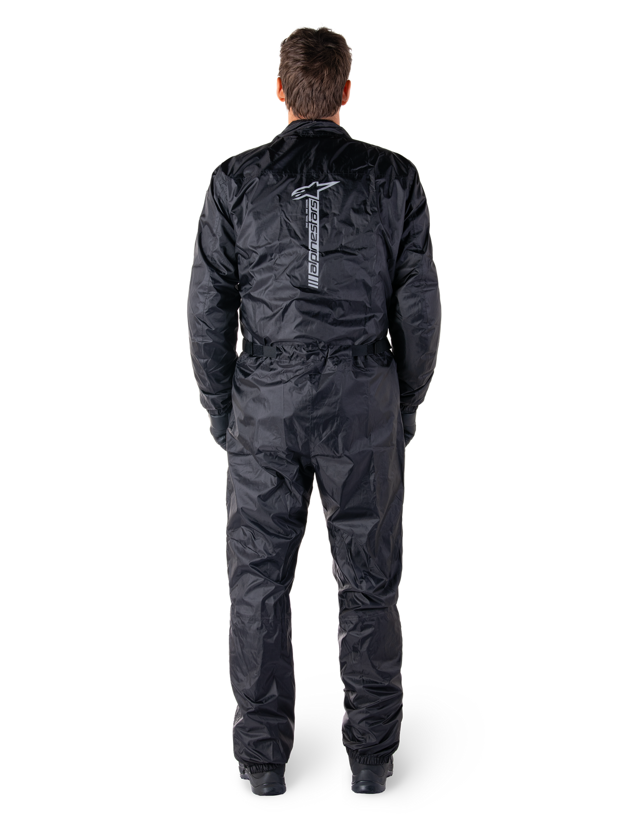 Alpinestars Hurricane Rain V2 Anzug, schwarzer einteiliger wasserdichter Motorrad-Regenanzug, Rückansicht mit großem vertikalem Alpinestars-Schriftzug und Logo, leichtes Gewebe mit elastischem Bund und Bündchen, konzipiert für Schutz bei nassem Wetter.