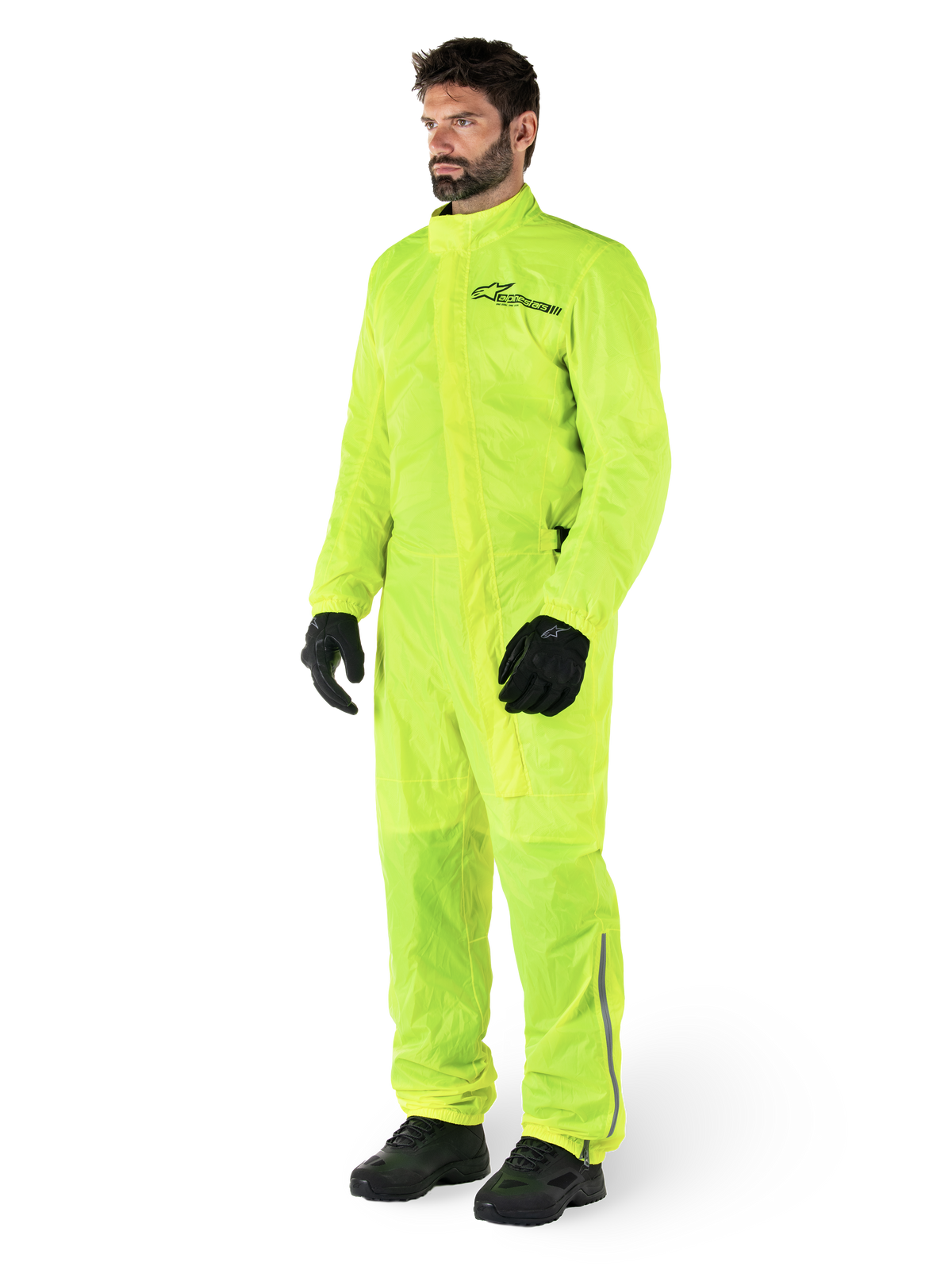 Alpinestars Hurricane Rain V2 Anzug, einteiliger wasserdichter Motorrad-Regenanzug, Gelb Fluo, getragen mit schwarzen Handschuhen und Stiefeln, mit schwarzem Alpinestars-Logo auf der Brust und reflektierenden Details an den Beinen