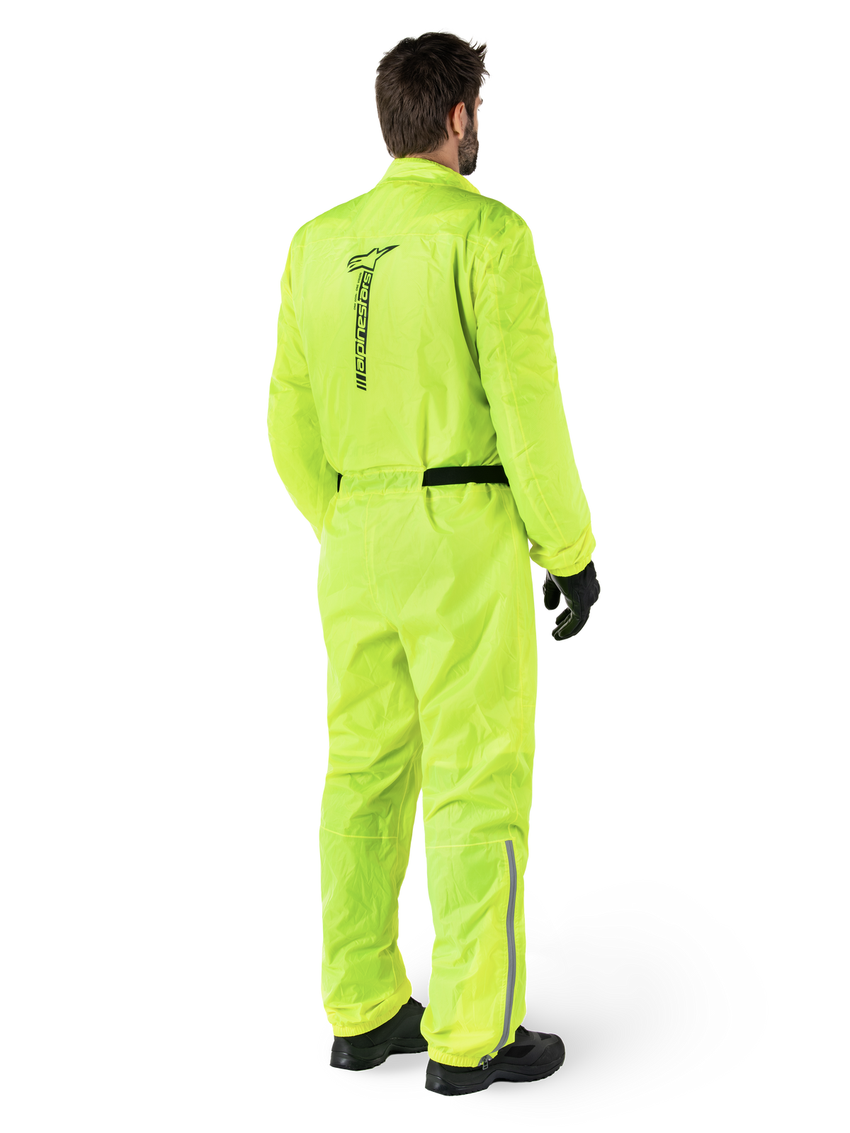 Alpinestars Hurricane Rain V2 Anzug, Gelb Fluo, Rückansicht eines Fahrers in einem einteiligen Motorrad-Regenanzug, mit schwarzem Alpinestars-Logo auf dem Rücken, schwarzem Hüftgurt und reflektierenden Streifen an den Unterschenkeln, getragen mit schwarzen Handschuhen und Stiefeln