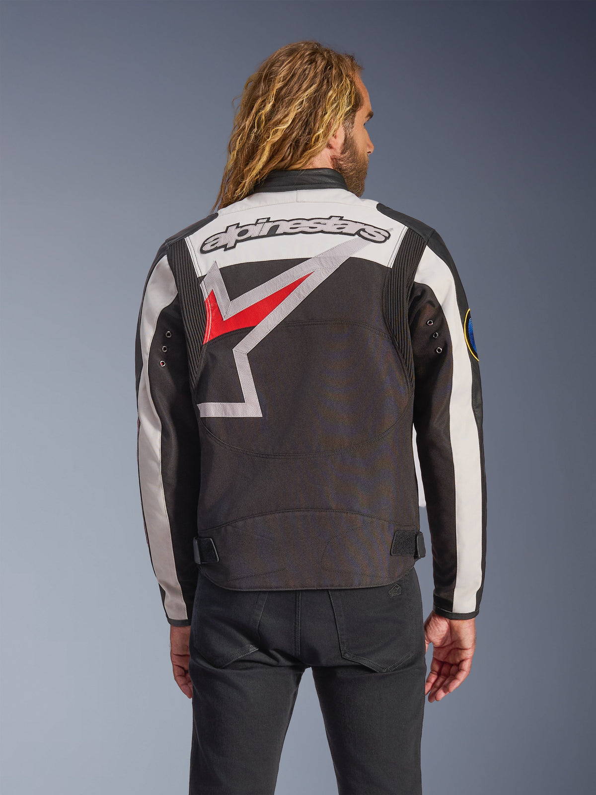 Alpinestars Axton Jacke, Motorradjacke, Schwarz, Off-White und Hellrot, Rückansicht mit großem, umlaufendem Stern-Logo und Wortmarke, von Vintage-Rennsport inspiriertes Design mit Akkordeon-Paneelen an den Schultern und Taillenverstellern