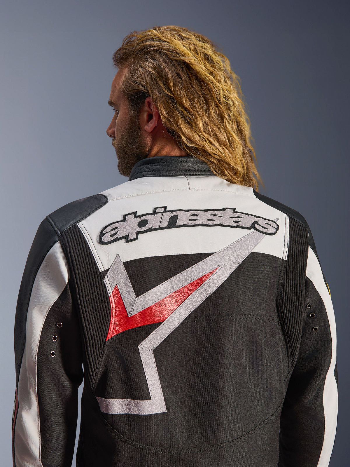 Alpinestars Axton Jacke, Motorradjacke, Schwarz, Off-White und Bright Red, Rückansicht mit großem besticktem Alpinestars-Logo und stilisierter Grafik, Akkordeon-Paneele an den Schultern für Bewegungsfreiheit, Vintage-inspiriertes Design mit Metallösen-Details