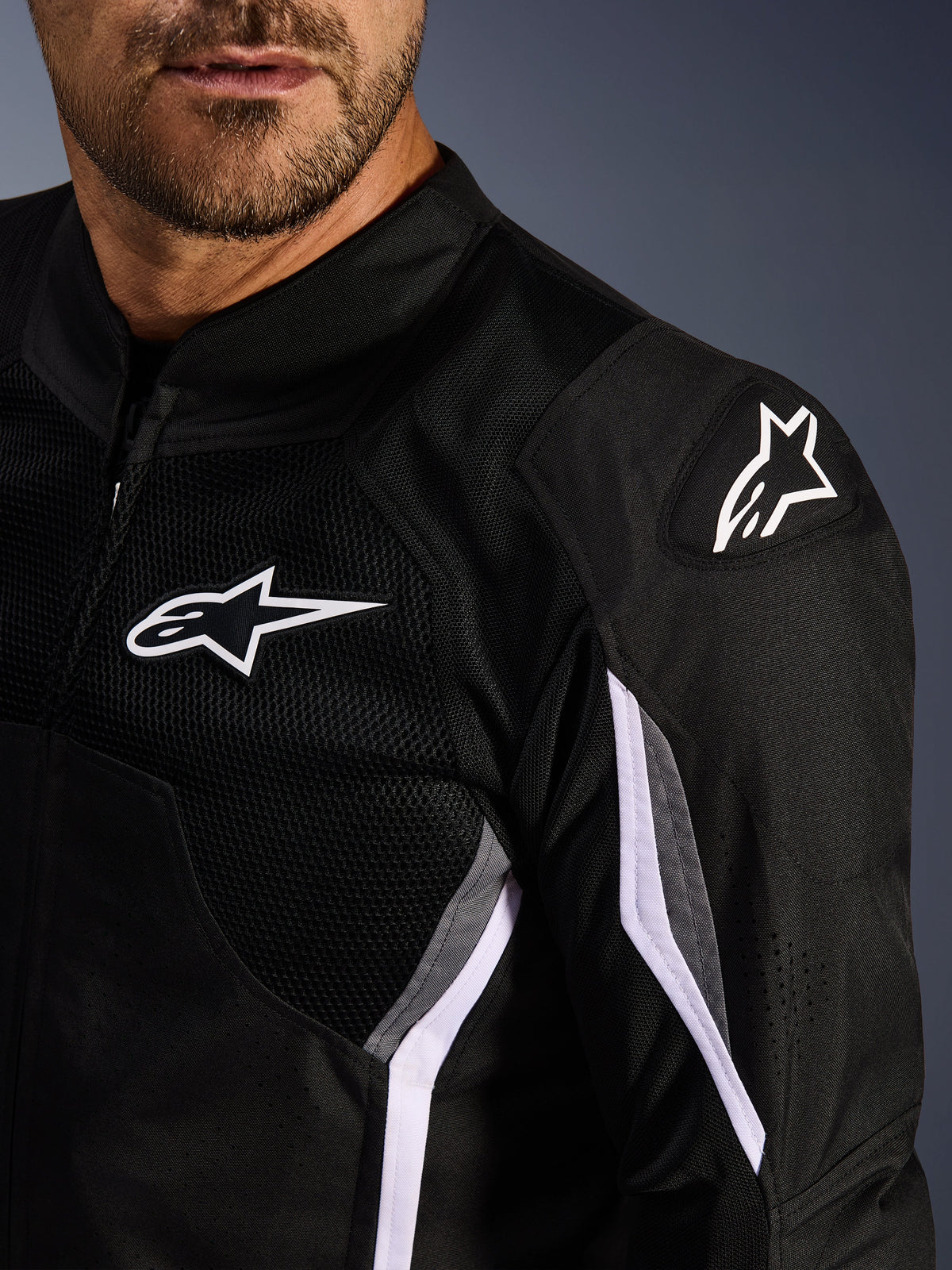 Alpinestars AST V3 Air Jacke, Textil-Motorradjacke, Schwarz Dunkelgrau Weiß, Nahaufnahme mit Mesheinsätzen, weißem Alpinestars-Logo auf Brust und Schulter und externen DFS GP Lite Evo Schulterschleifern