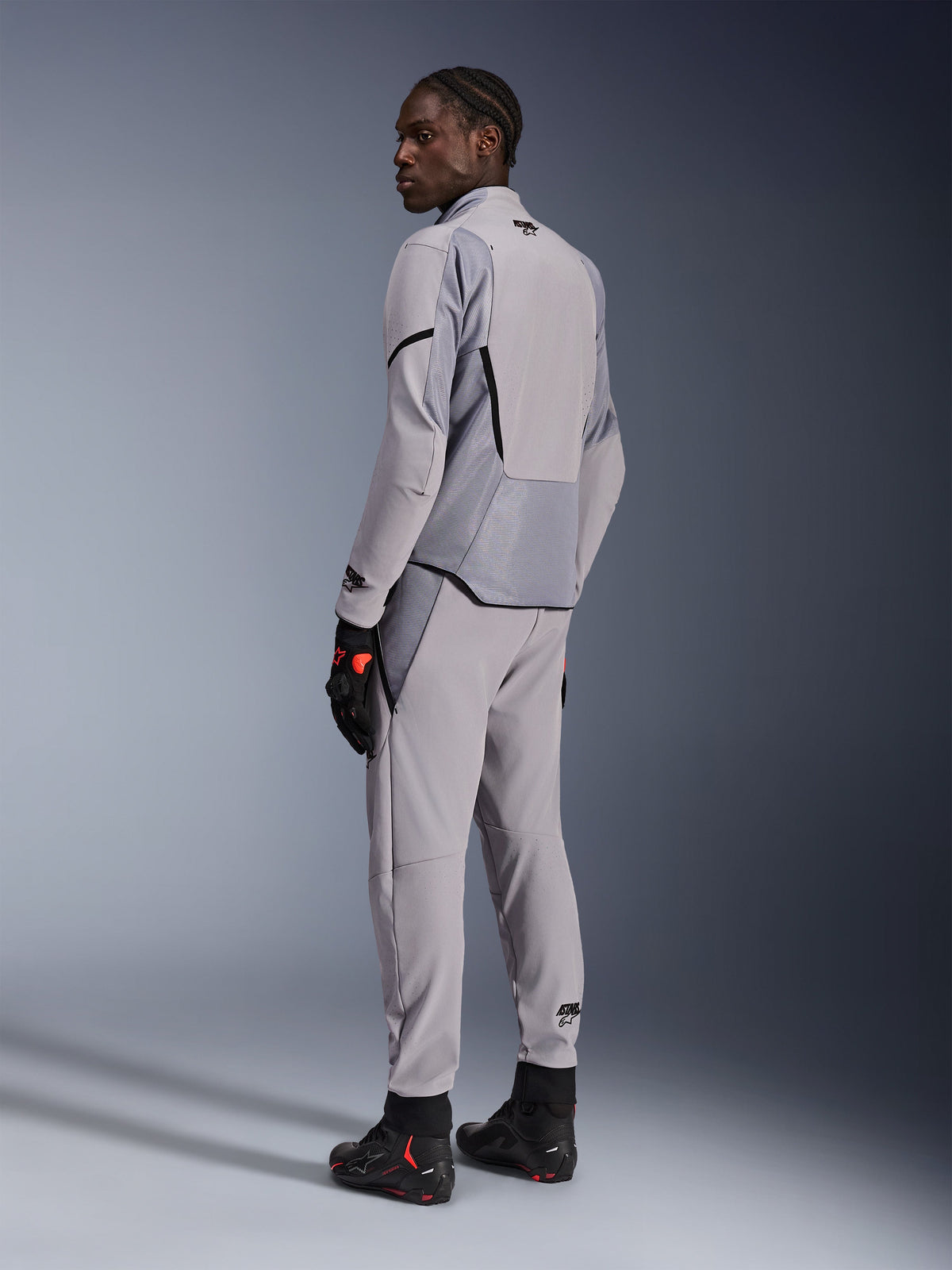 Alpinestars Aeroshell Airflow Jacke in Mid Gray Anthracite, kombiniert mit passender Hose und schwarzen Rennhandschuhen, Rückansicht mit laserperforierten Paneelen und athletischer Sportpassform, professionelle Motorradbekleidung