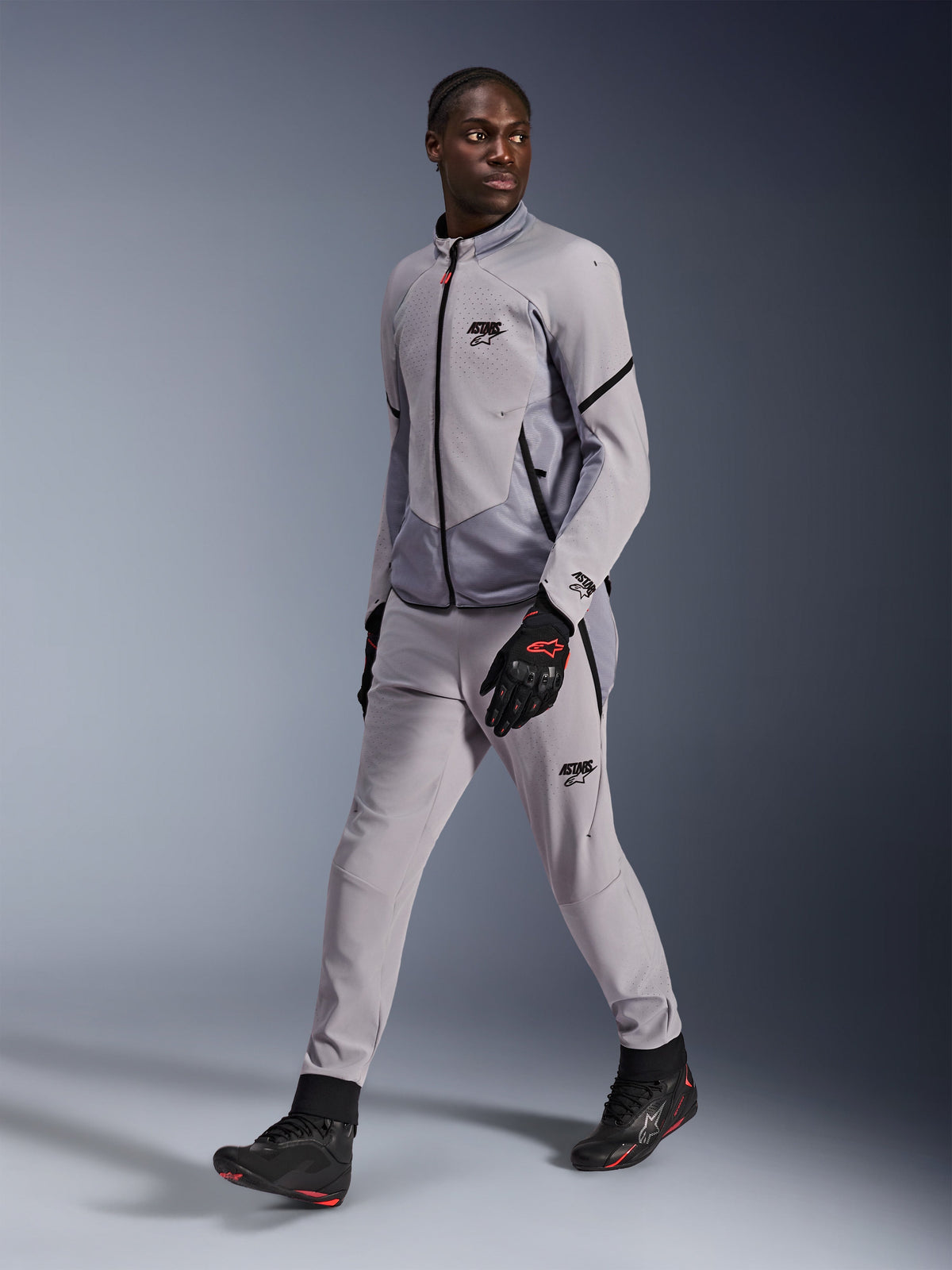 Alpinestars Aeroshell Airflow Jacke in Mittelgrau Anthrazit, getragen von einem männlichen Model mit passender grauer Motorradhose und schwarzen Handschuhen, laserperforierte Brustbelüftung, sportliches Design