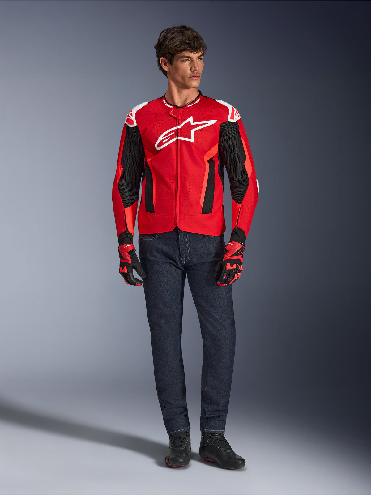Alpinestars T-GP Air Jacket, Bright Red Red Fluo Black, male model wearing full motorcycle outfit with dark blue jeans and matching gloves, sport textile jacket featuring perforated mesh panels and white Astars logo, studio shot.