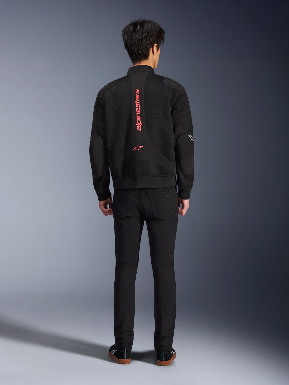Alpinestars Flight Air Jacket in Black Bright Red, Rear view of urban bomber-style motorcycle jacket, featuring vertical red Alpinestars branding and logo on the spine, lightweight 3D mesh construction, worn with black pants for a contemporary look.