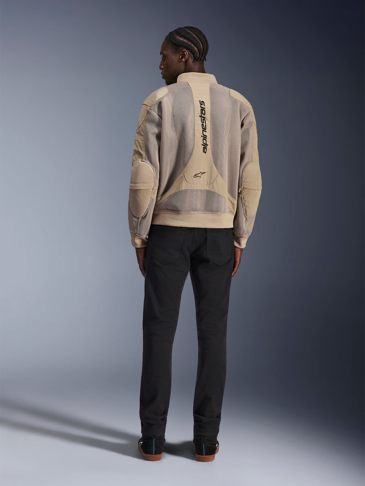 Alpinestars Flight Air Jacke, sandfarbene urbane Motorradjacke, Rückansicht mit atmungsaktiven 3D-Mesh-Paneelen und vertikalem Logo, getragen mit einer schwarzen Hose für einen modernen Streetstyle-Look
