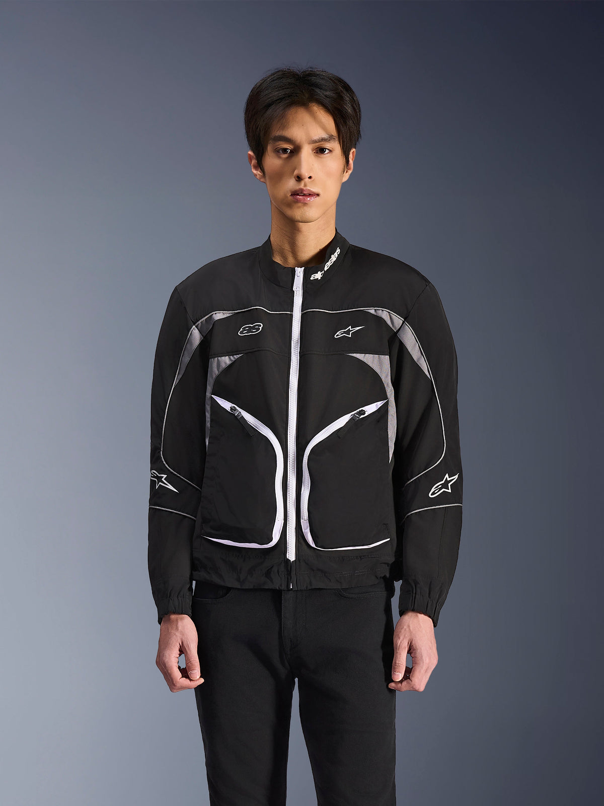 Alpinestars Unite Jacke, minimalistische urbane Motorradjacke, Schwarz und Dunkelgrau mit weißen Akzenten, weißer Frontreißverschluss, reflektierende Paspeln und Alpinestars-Branding auf Brust und Ärmeln, moderner Streetwear-Stil für Motorradfahrer