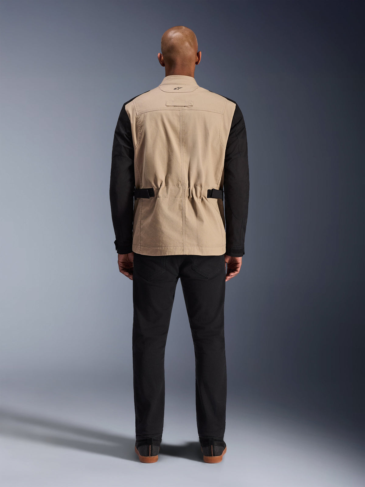 Alpinestars Dice Jacket, Urban Motorcycle Jacket, Tan and Black, Rear view on model, featuring polycotton twill construction, adjustable waist straps, and small embroidered logo on the collar, worn with black pants