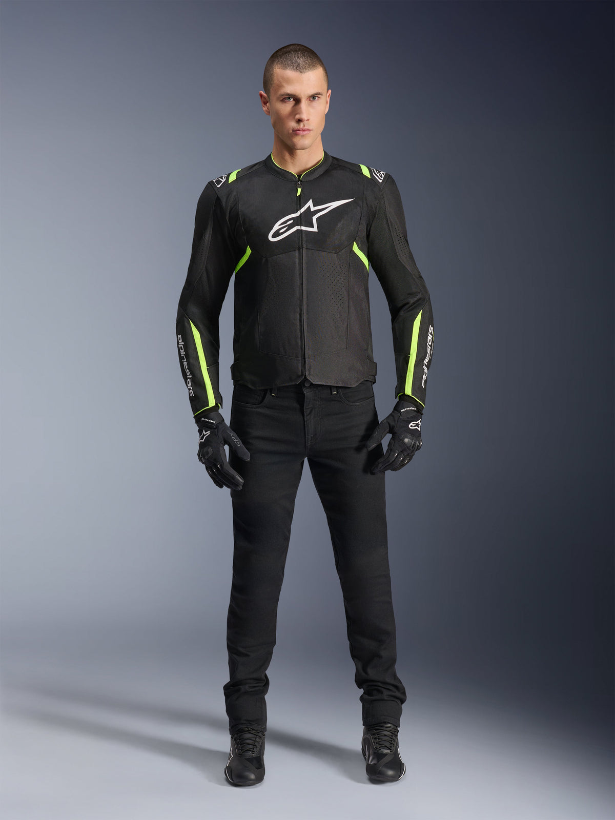 Alpinestars T-Sps Air V2 Jacke, Schwarz und Gelb Fluo, Textil-Motorradjacke mit Mesh-Einsätzen, getragen von einem männlichen Model mit schwarzer Hose und Handschuhen, weißes Alpinestars-Logo auf der Brust, urbane Sport-Motorradausrüstung
